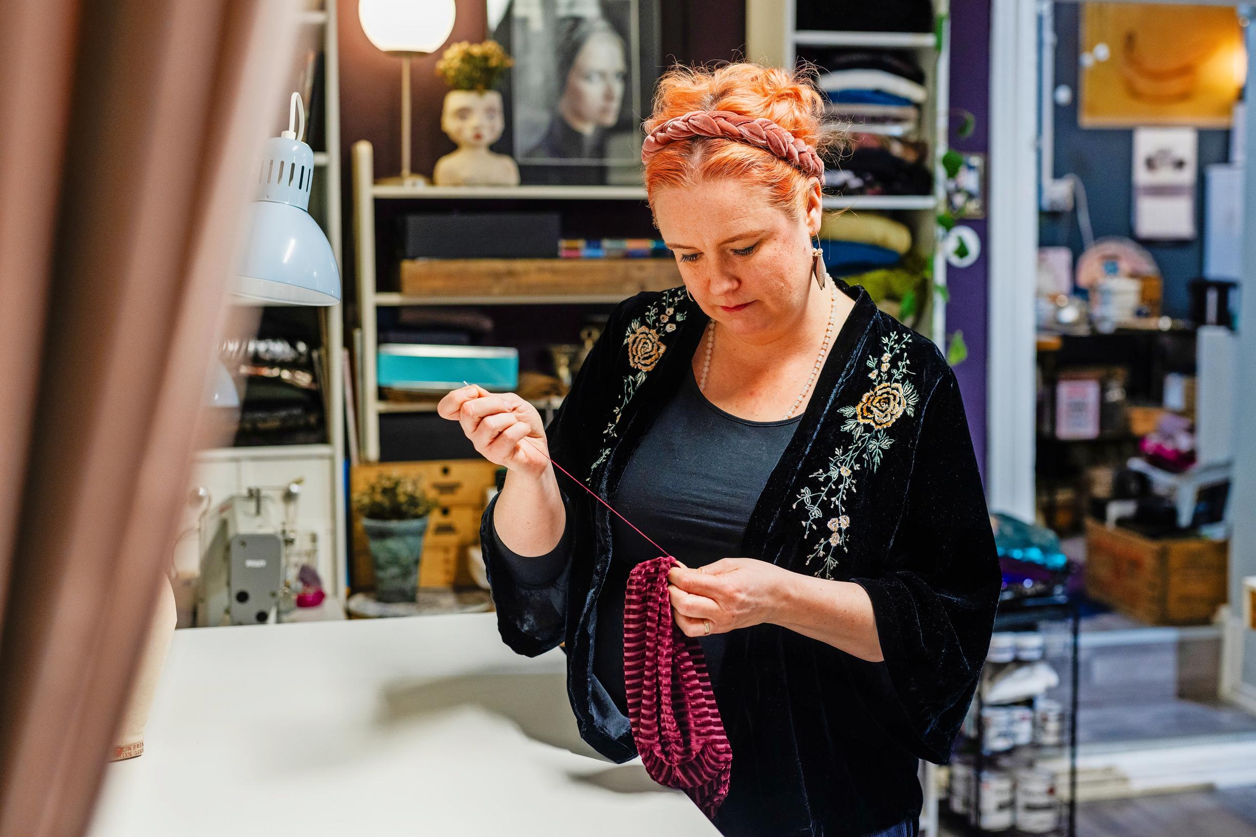 nainen ompelee käsin työpöydän äärellä