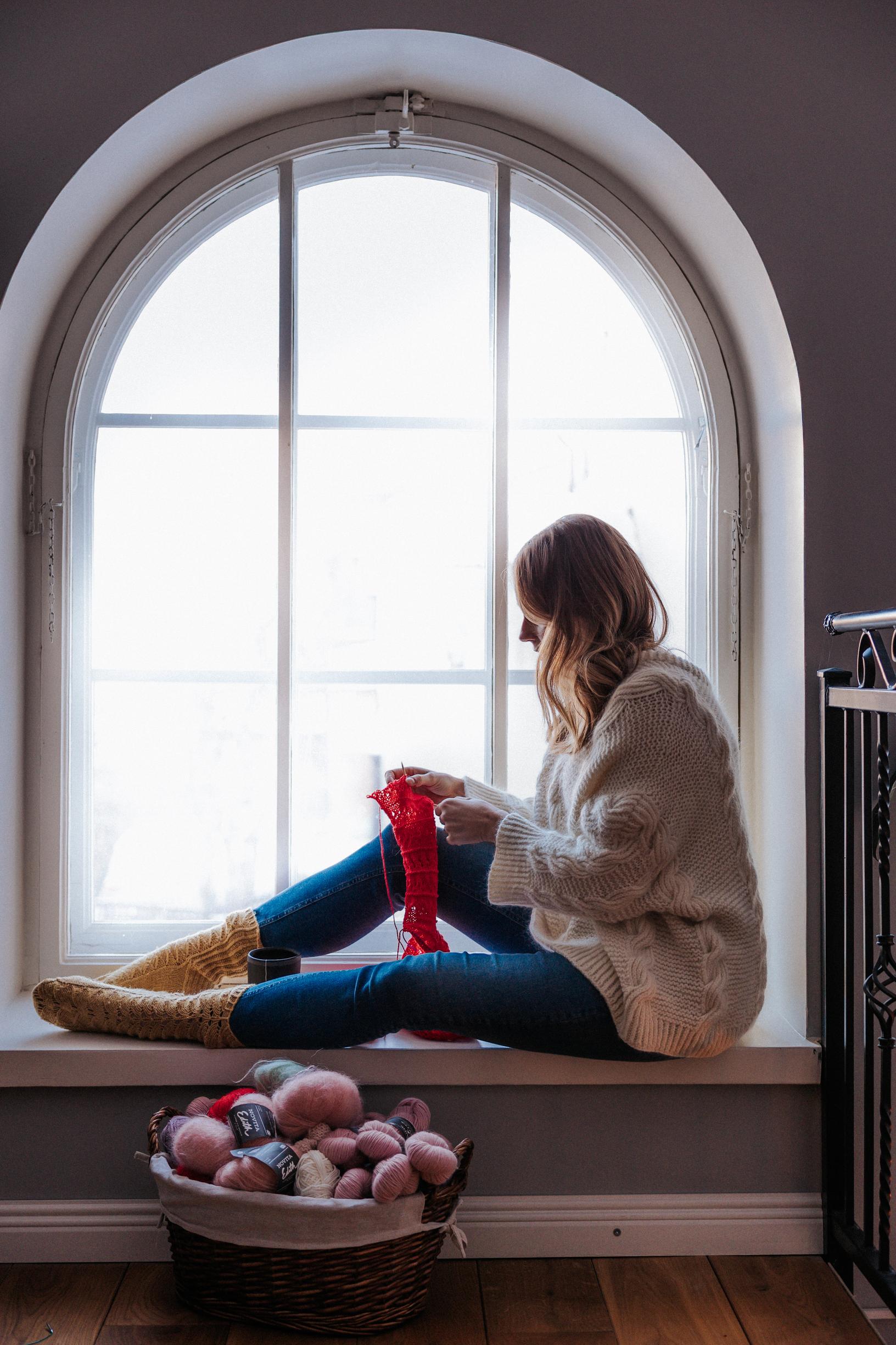 Marita Paasonen istuu ikkunan ääressä ja neuloo.