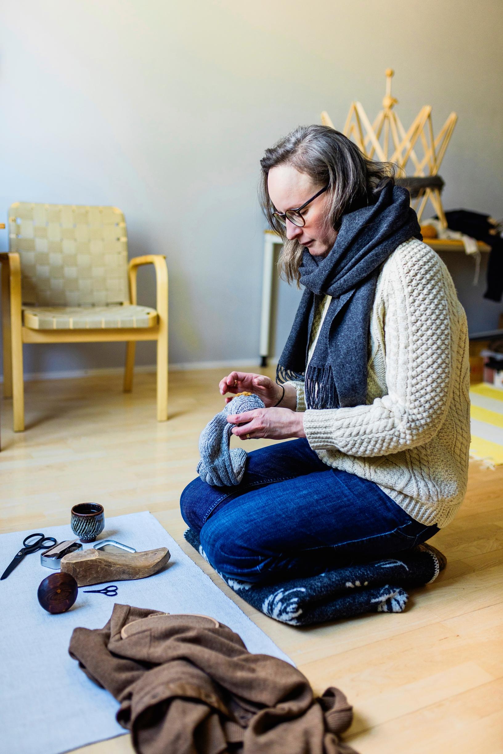 Minttu Wikberg istuu lattialla ja parsii sukkaa.