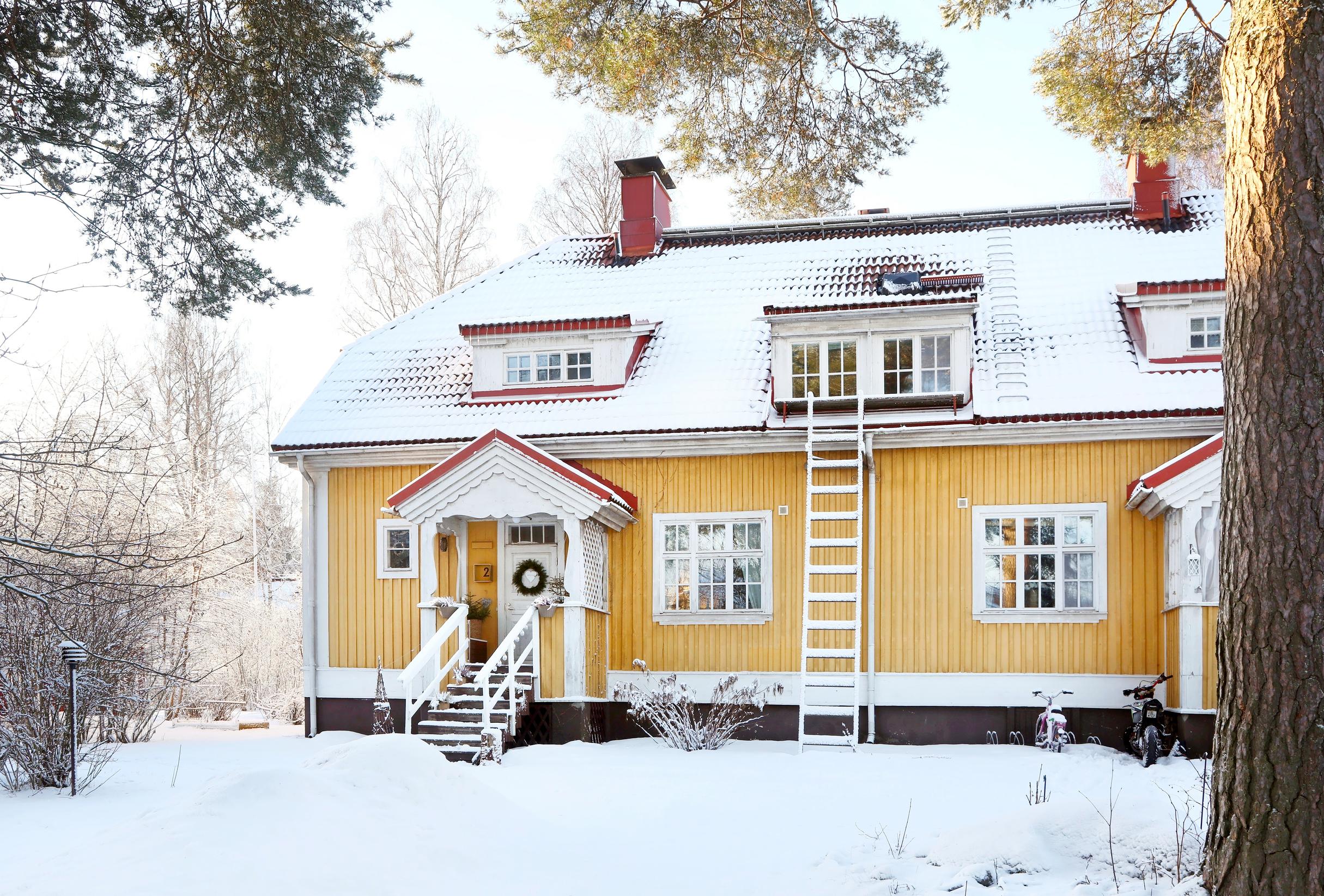 Keltaisen satavuotiaan puurivitalohuoneiston oveen on ripustettu havukranssi.