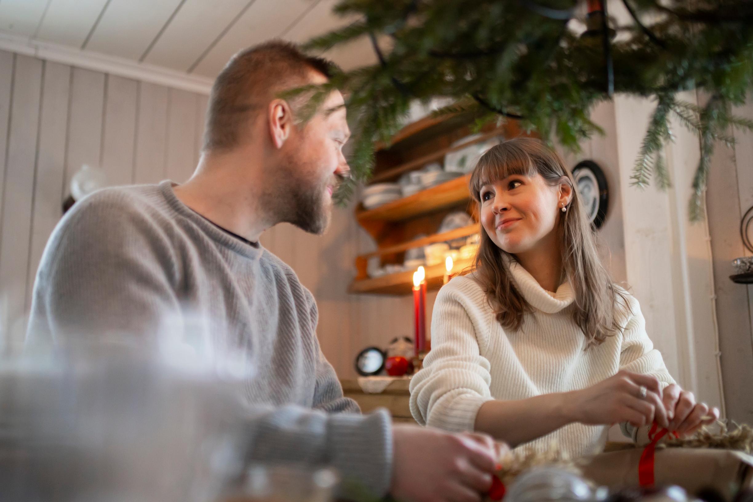 Pariskunta katsoo toisiaan istuen pöydän ääressä paketoimassa joululahjoja.