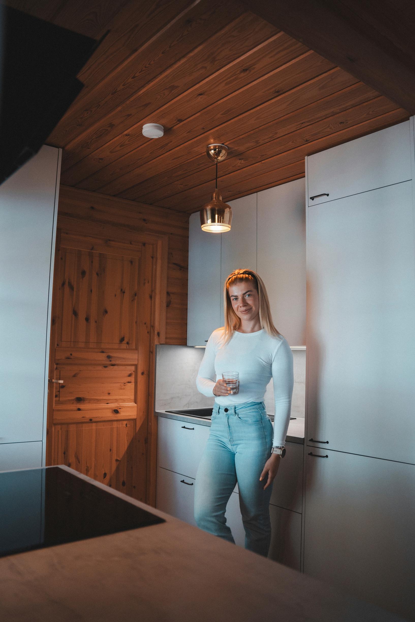 Pernilla Böckerman mökin keittiössä, valkoiset kaapit ja puuovi