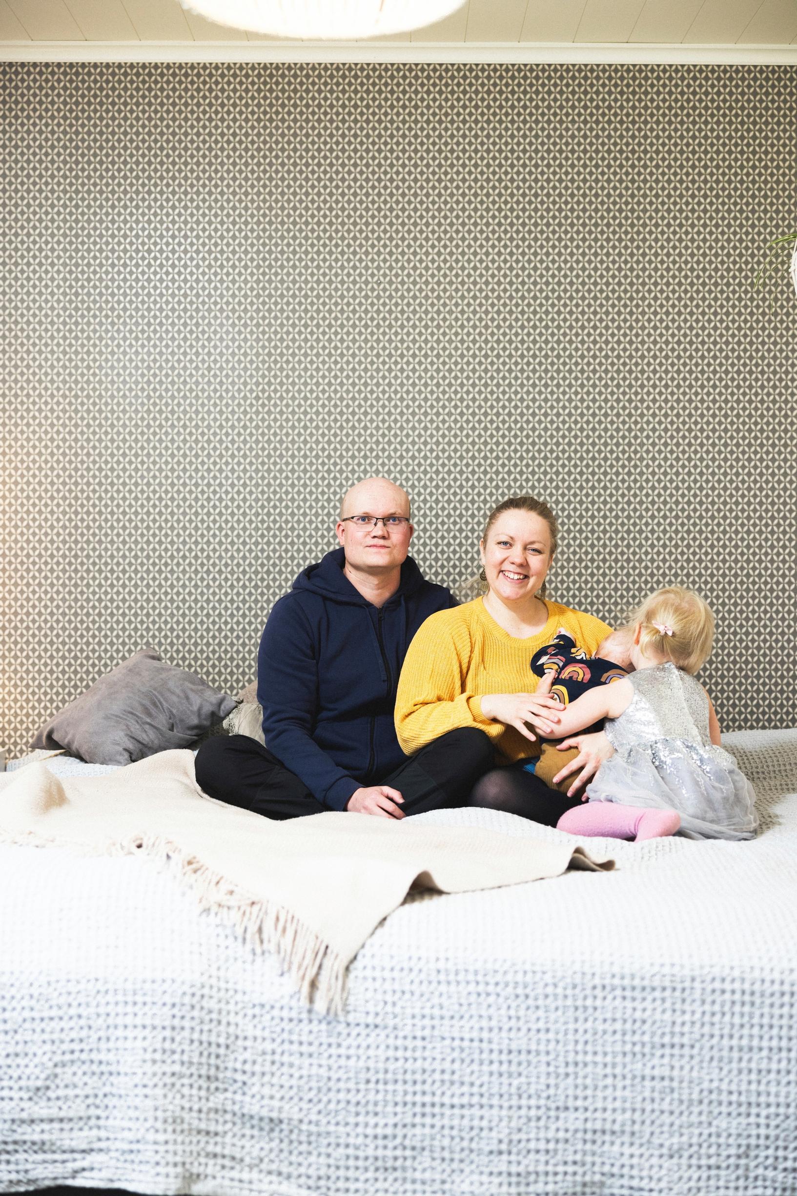 mies, nainen ja kaksi lasta istuvat sängyllä