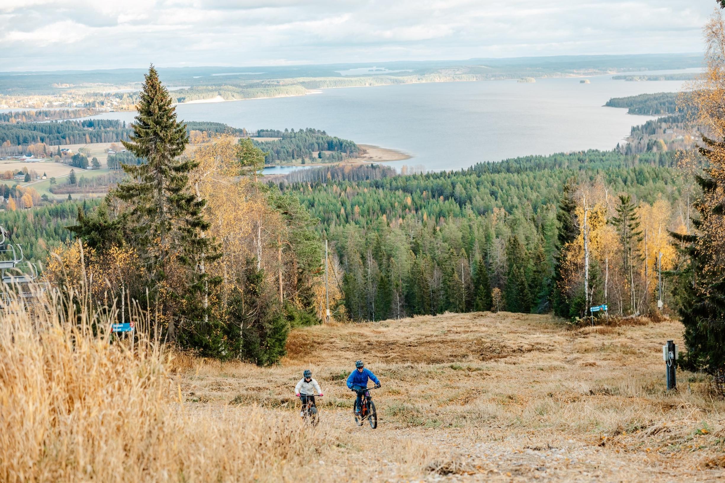 Kaksi pyöräilijää polkee ylös mäkeä, taustalla upea syksyinen maisema.