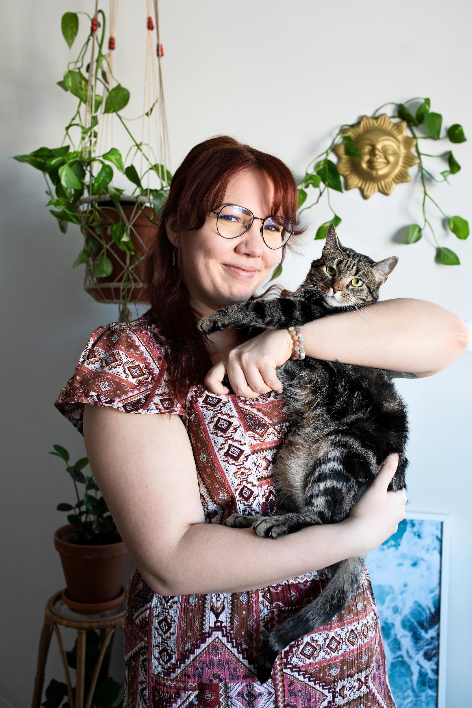 Raidallinen kissa naisen sylissä, seinällä viherkasvi kultaköynnös