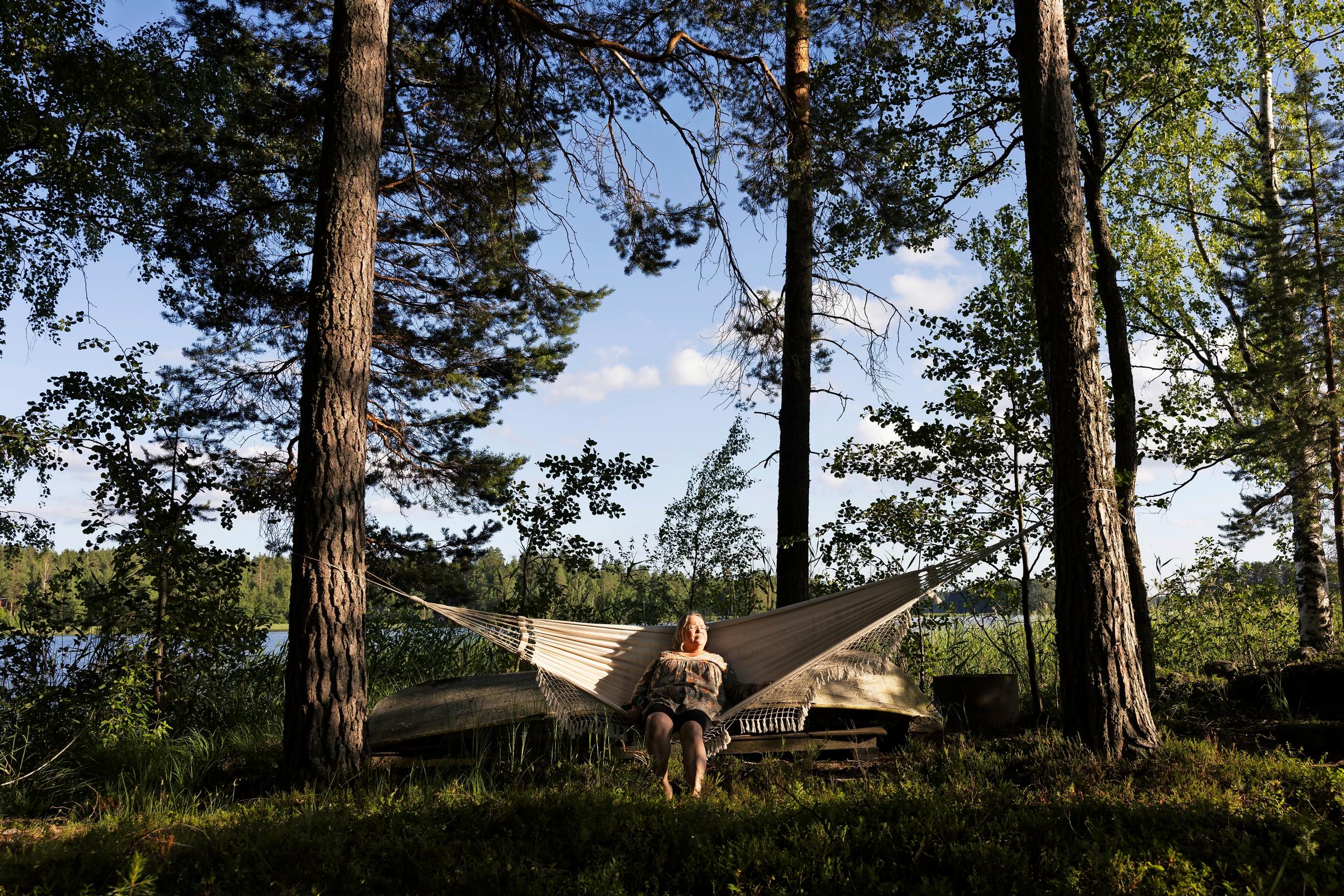 Helena istuu isossa riippukeinussa, suuria puita