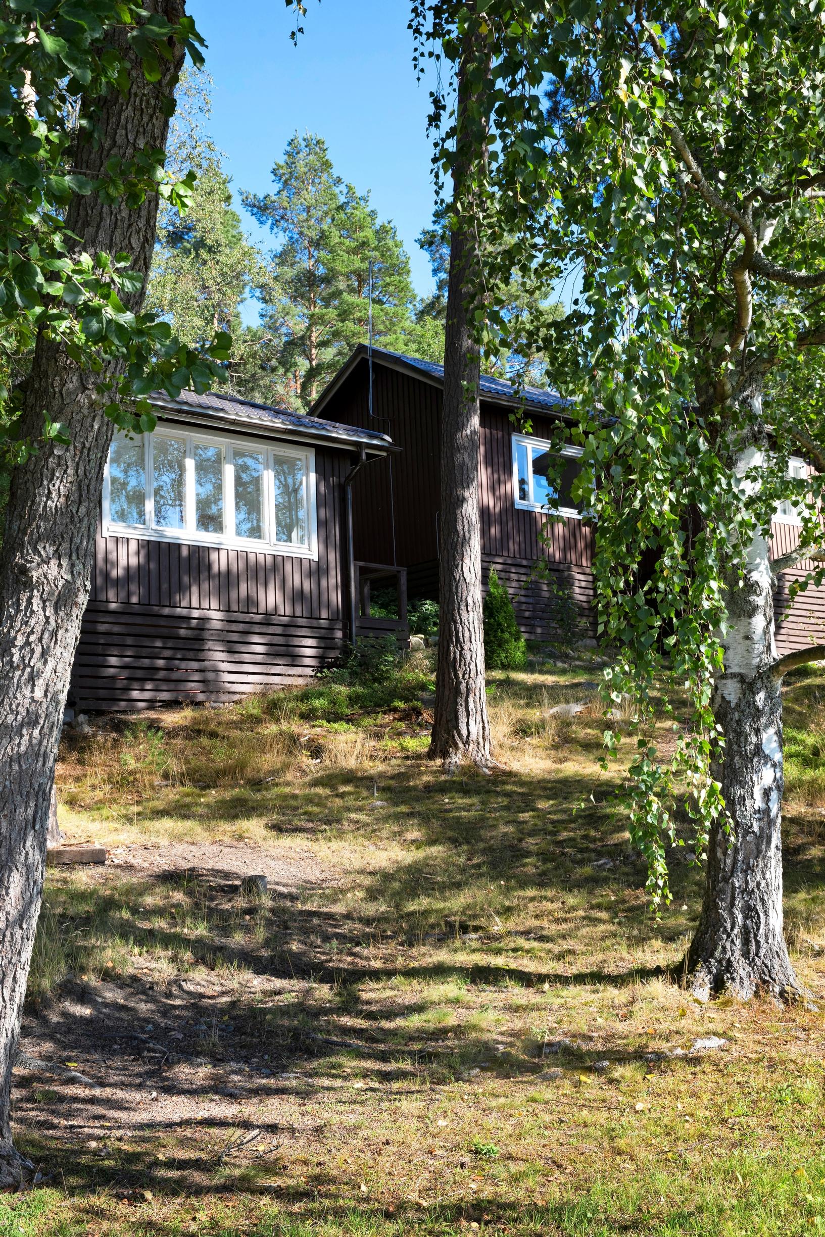 Ruskea kesämökki ja vierasmaja rinteessä.