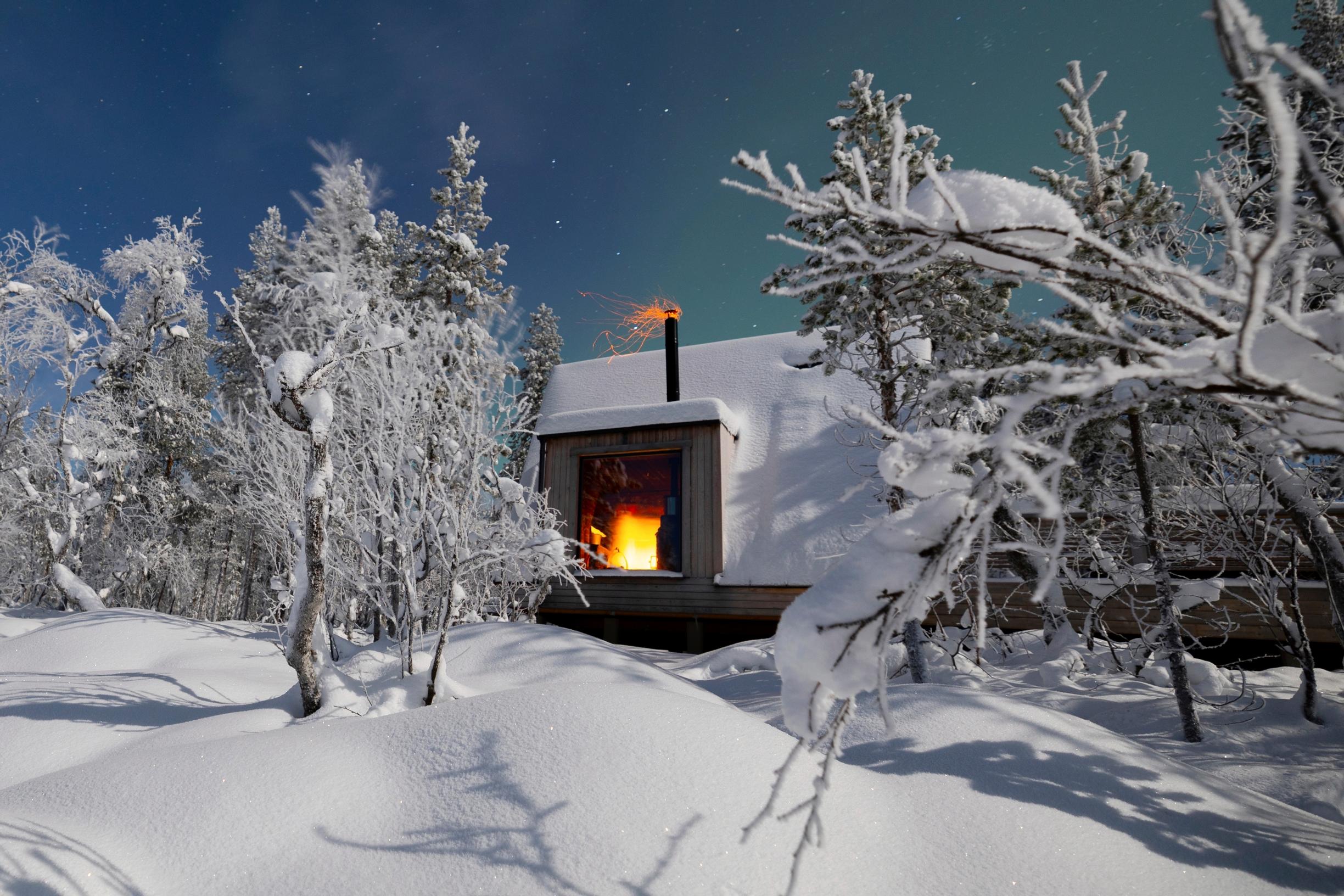 Lumikattoinen mökki maastoutuu talvimaisemaan