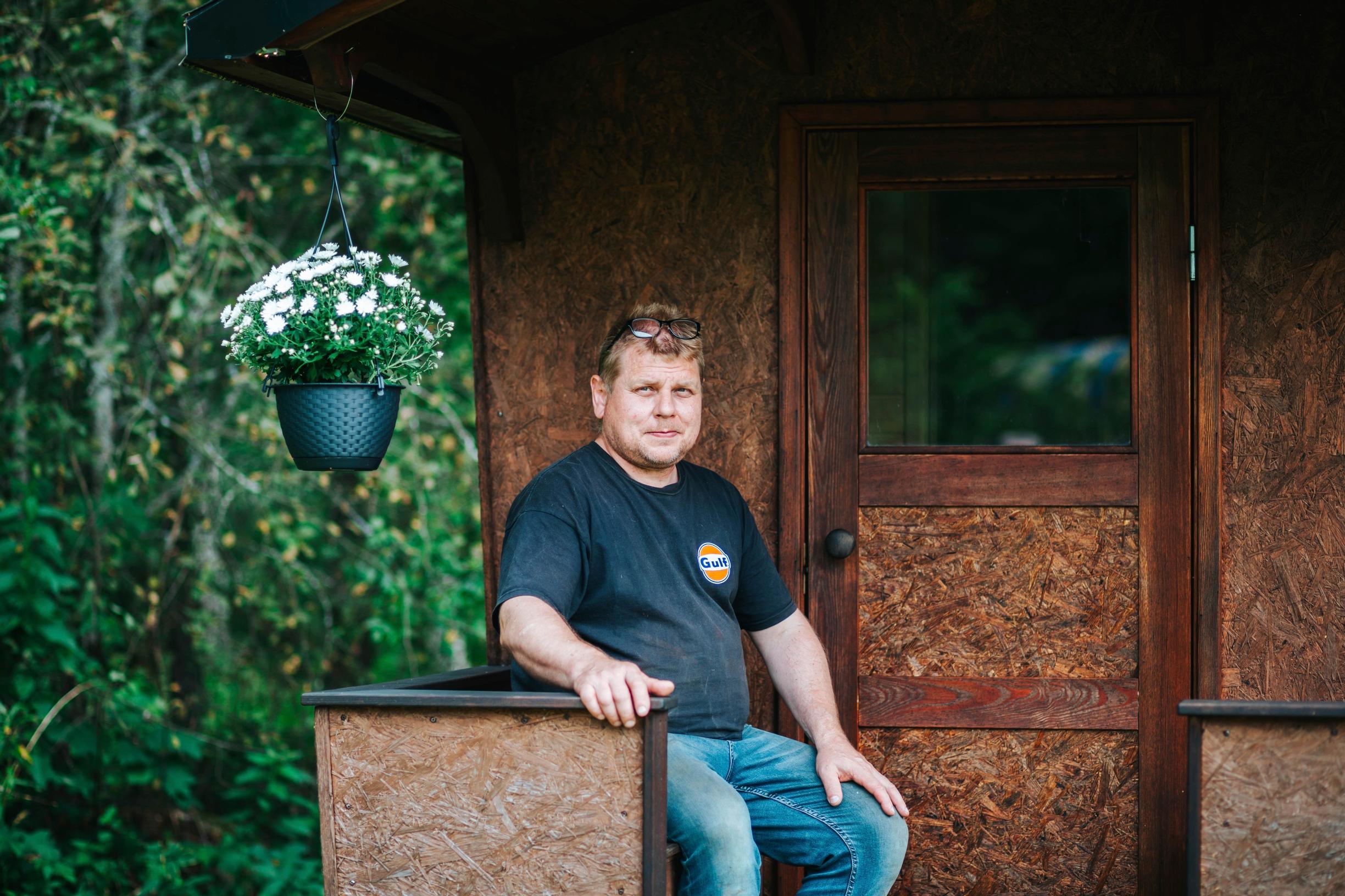 terho liukkonen istuu vankkurisaunan terassilla, kukka-amppeli vieressä