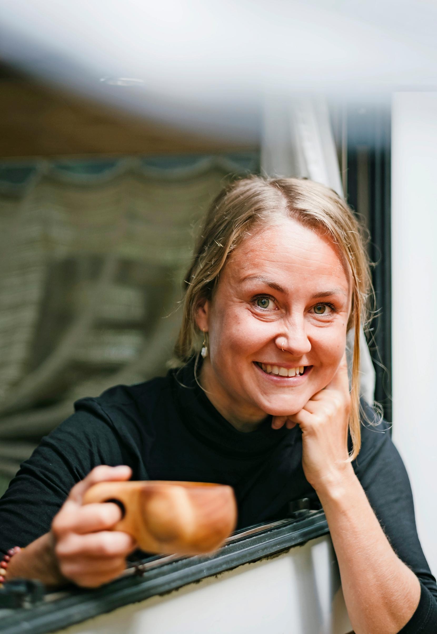 nainen katsoo ulos asuntoauton ikkunasta kuksa kädessään