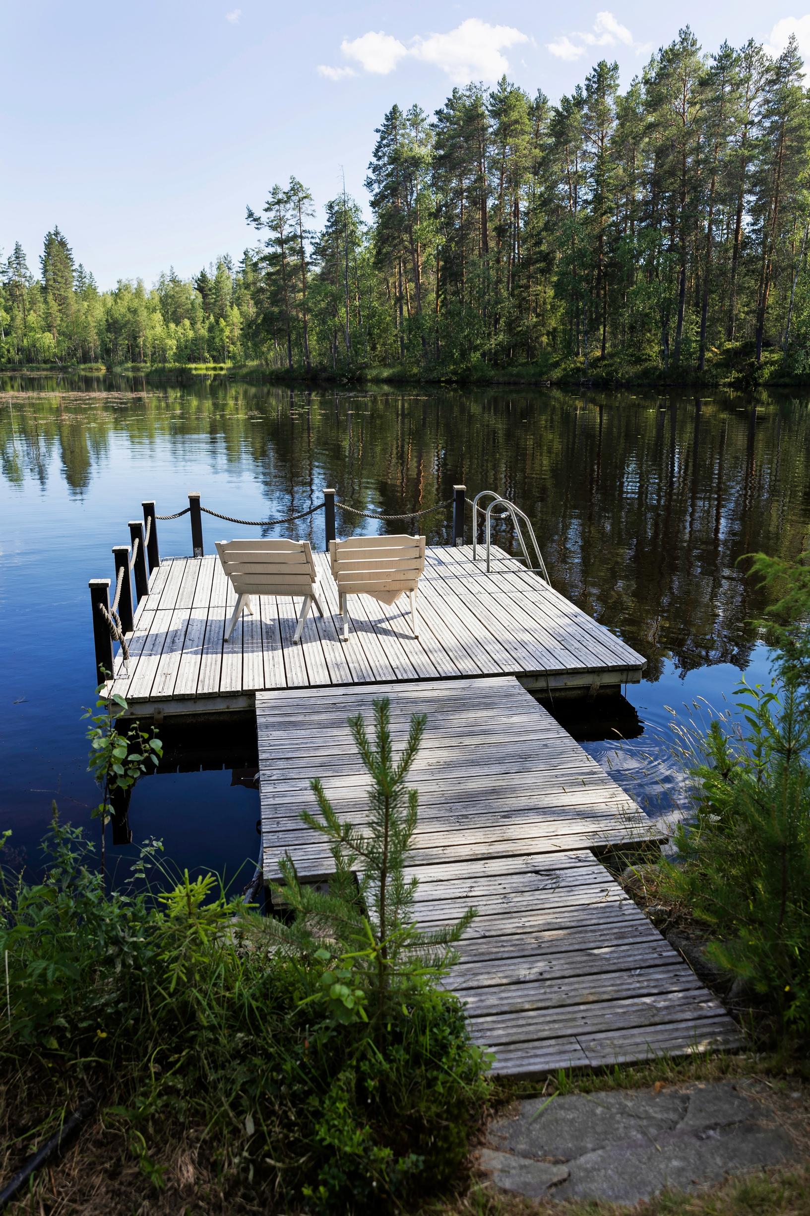 kaksi aurinkotuolia laiturilla, vastarannalla metsää
