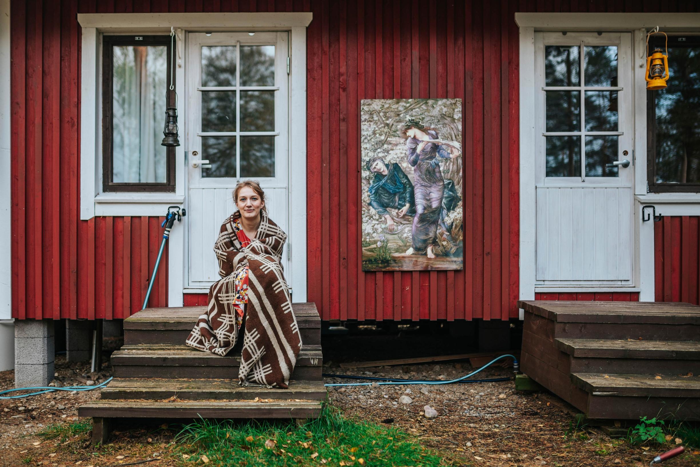 nainen istuu aitan portailla viltin sisällä