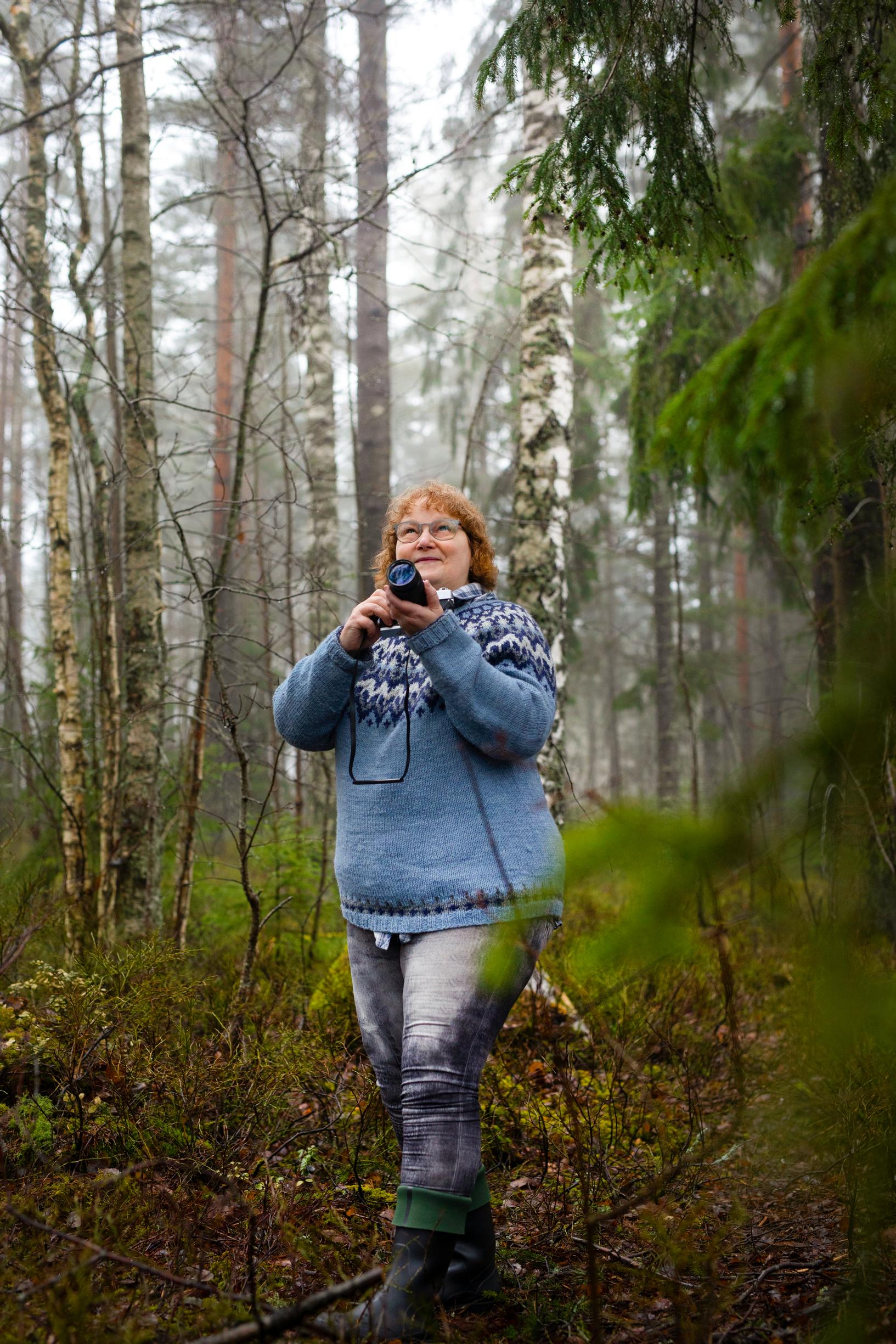 nainen seisoo metsässä kamera kädessään