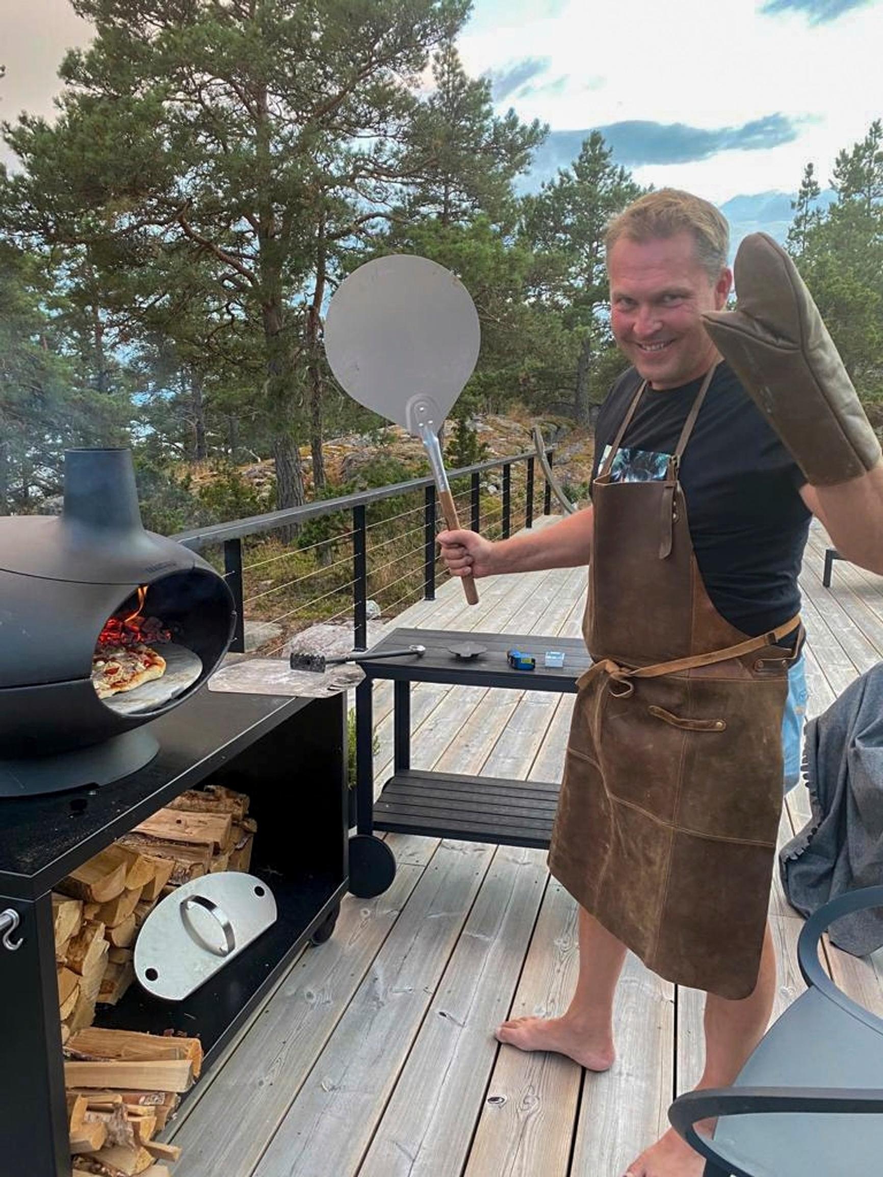 Jani Vahvanen patakinnas ja pizzalasta kädessä mökin terassilla pizzauunin edessä