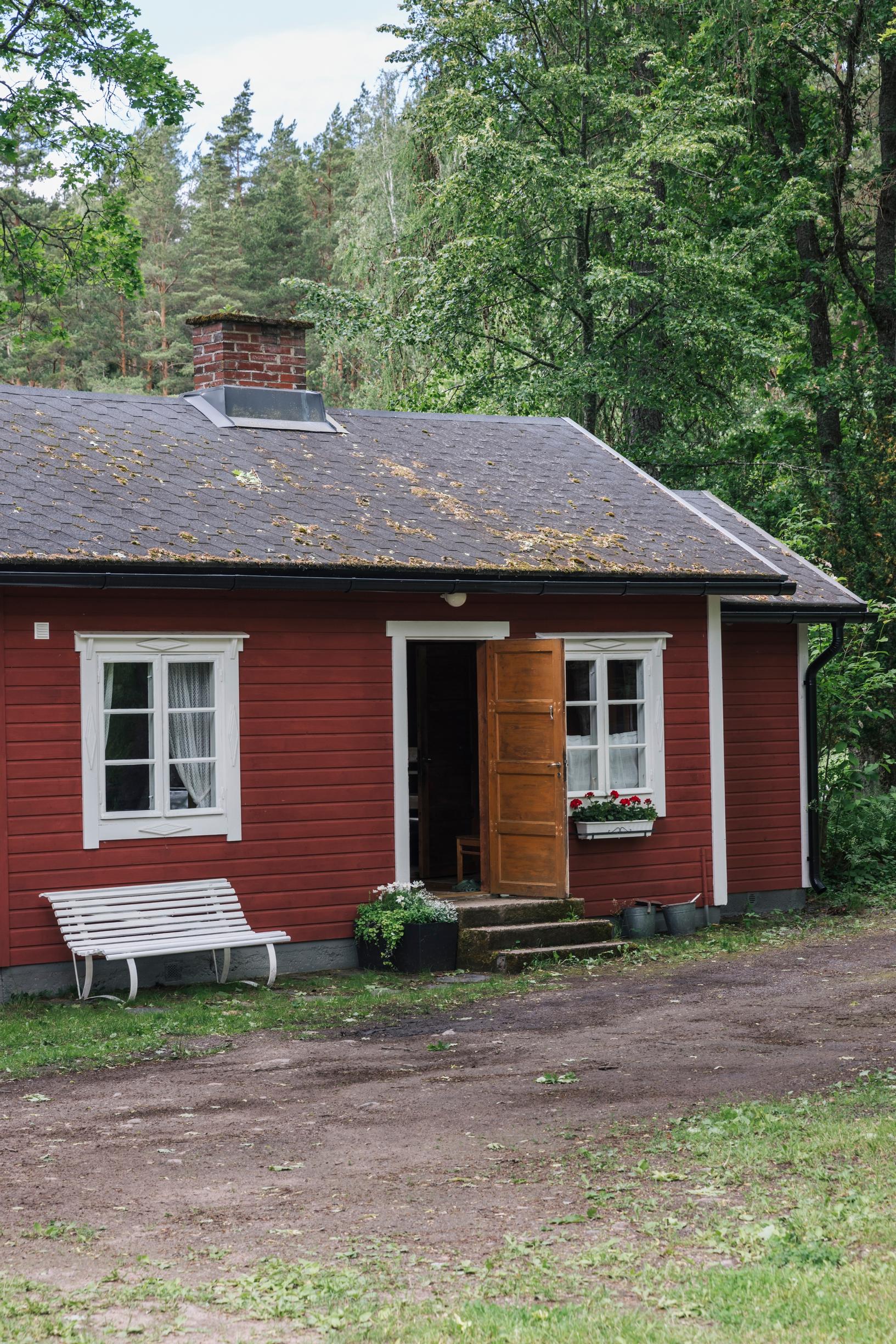 punainen piharakennus, ovi auki ja talon vieressä valkoinen penkki