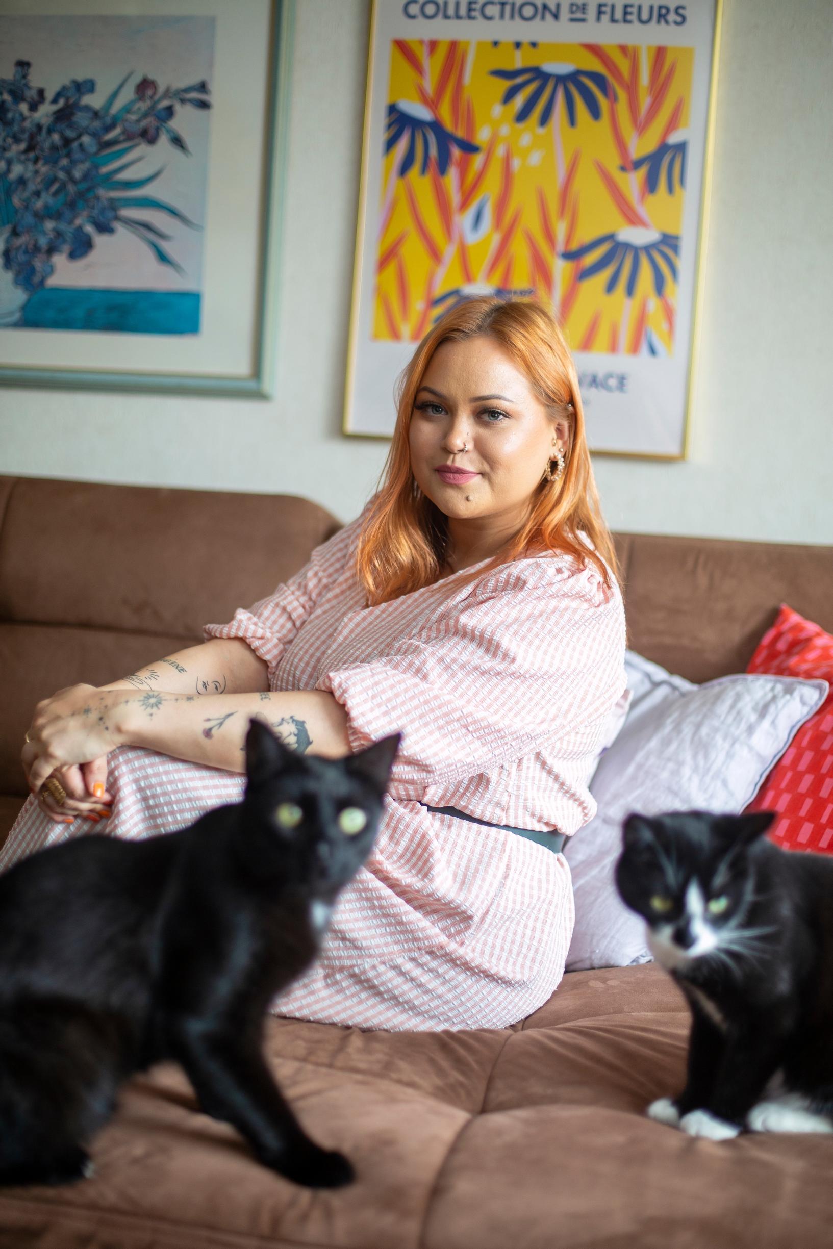 Nelli Alho istuu sohvalla kissojen kanssa