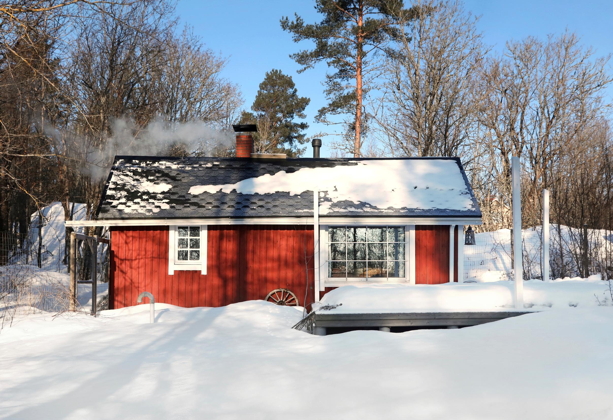 punainen pihasauna hangen keskellä, musta katto ja valkoiset ikkunanpielet