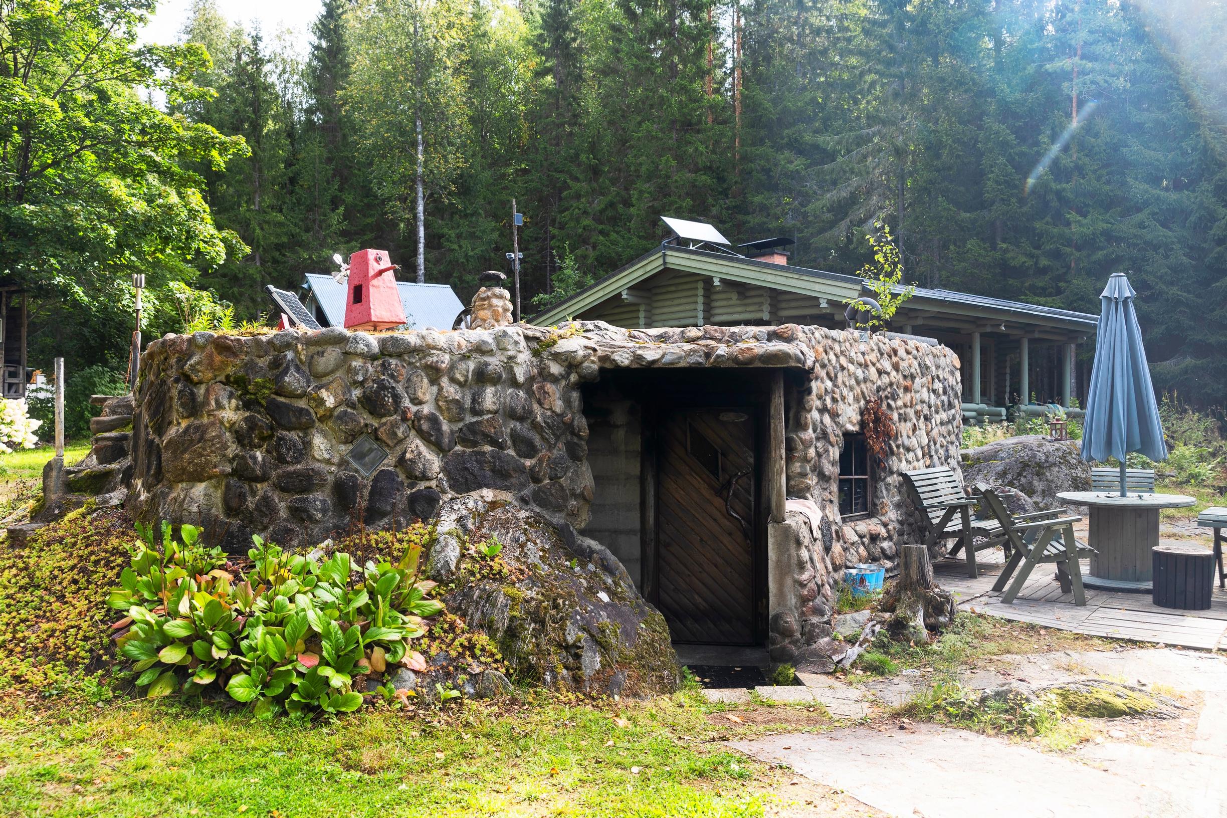 luonnonkivistä muurattu sauna, vuorenkilpiä, taustalla saunamökki, vieressä puutarharyhmä