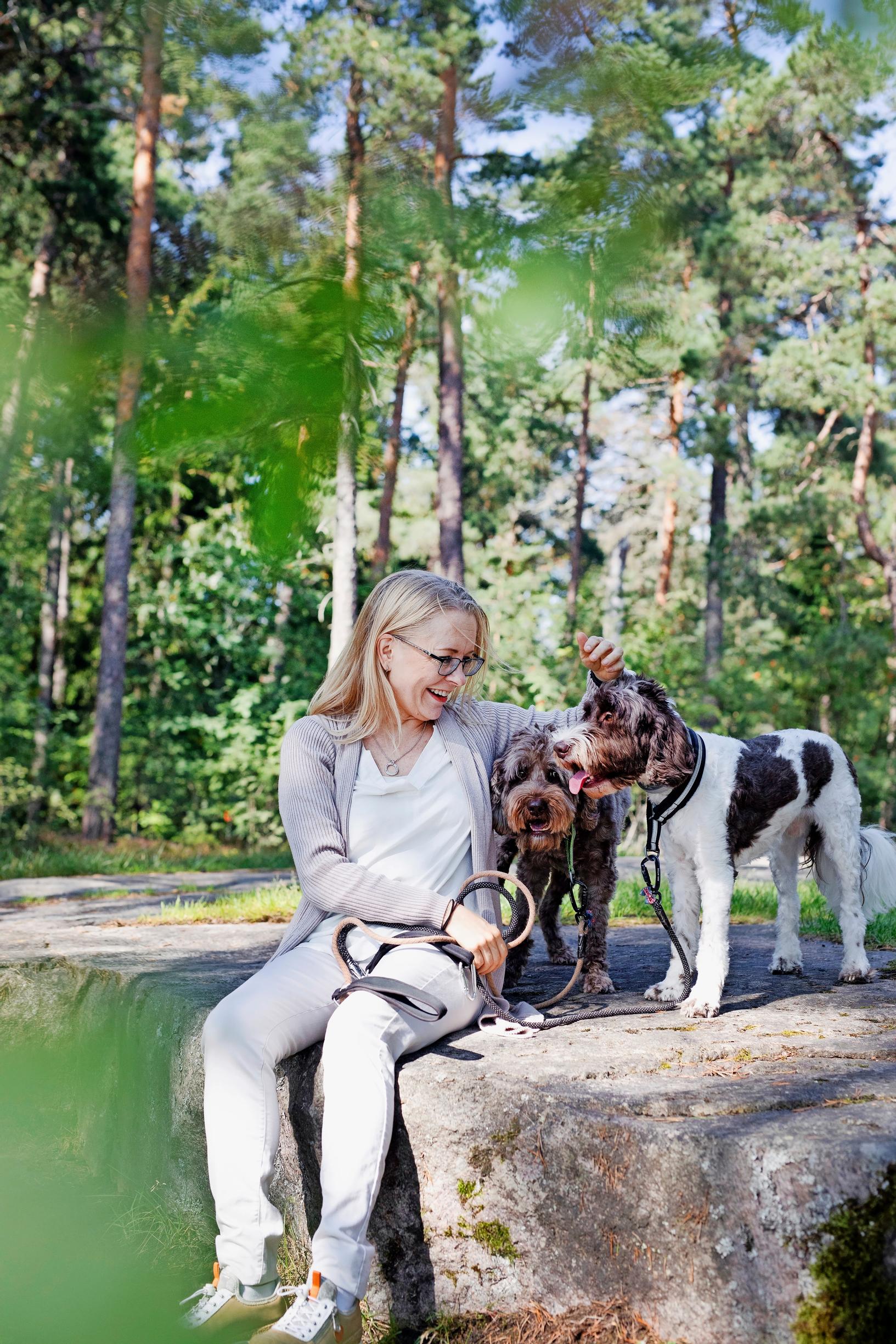 nainen istuu kivellä ja rapsuttaa kahta koiraansa