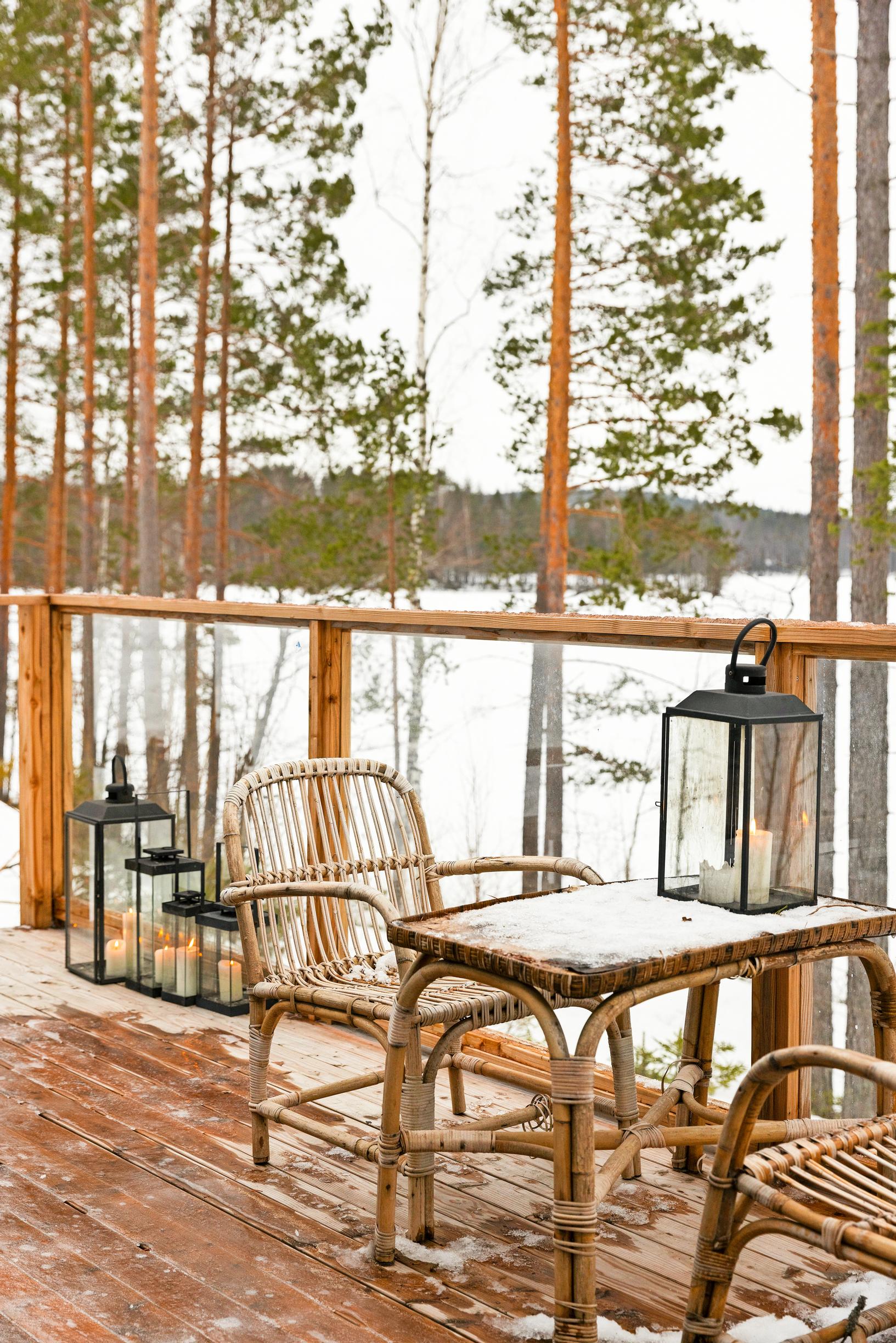 rottinkinen pöytäryhmä terassilla ja lyhtyjä, näkymä lumiselle järvelle