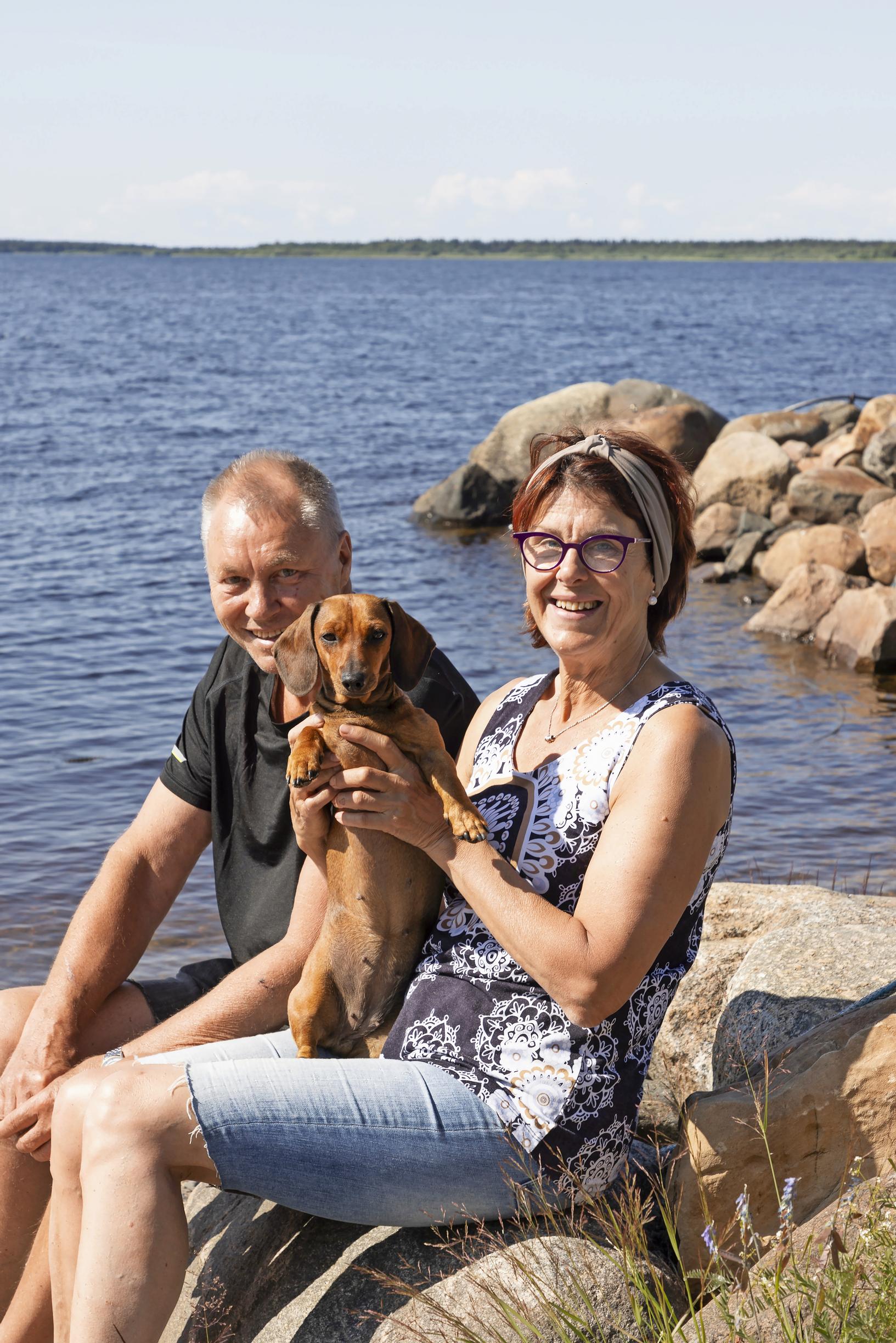 Marita Kumpulainen ja Eki Nikkanen saarimökin rannassa Selkäsaarella, sylissä mäyräkoira