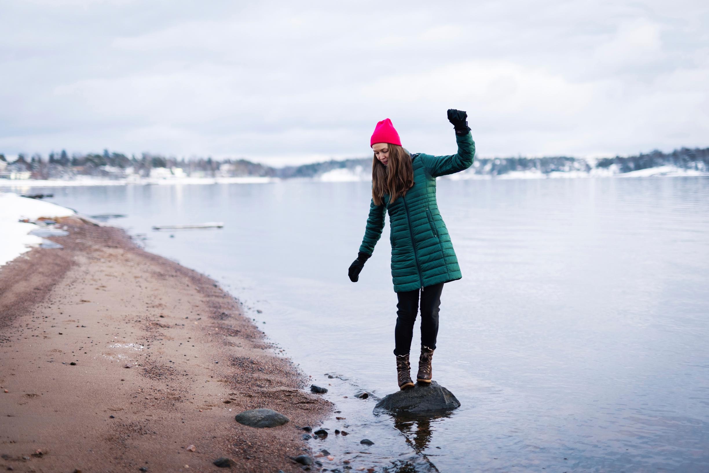 nainen seisoo kivellä rantavedessä