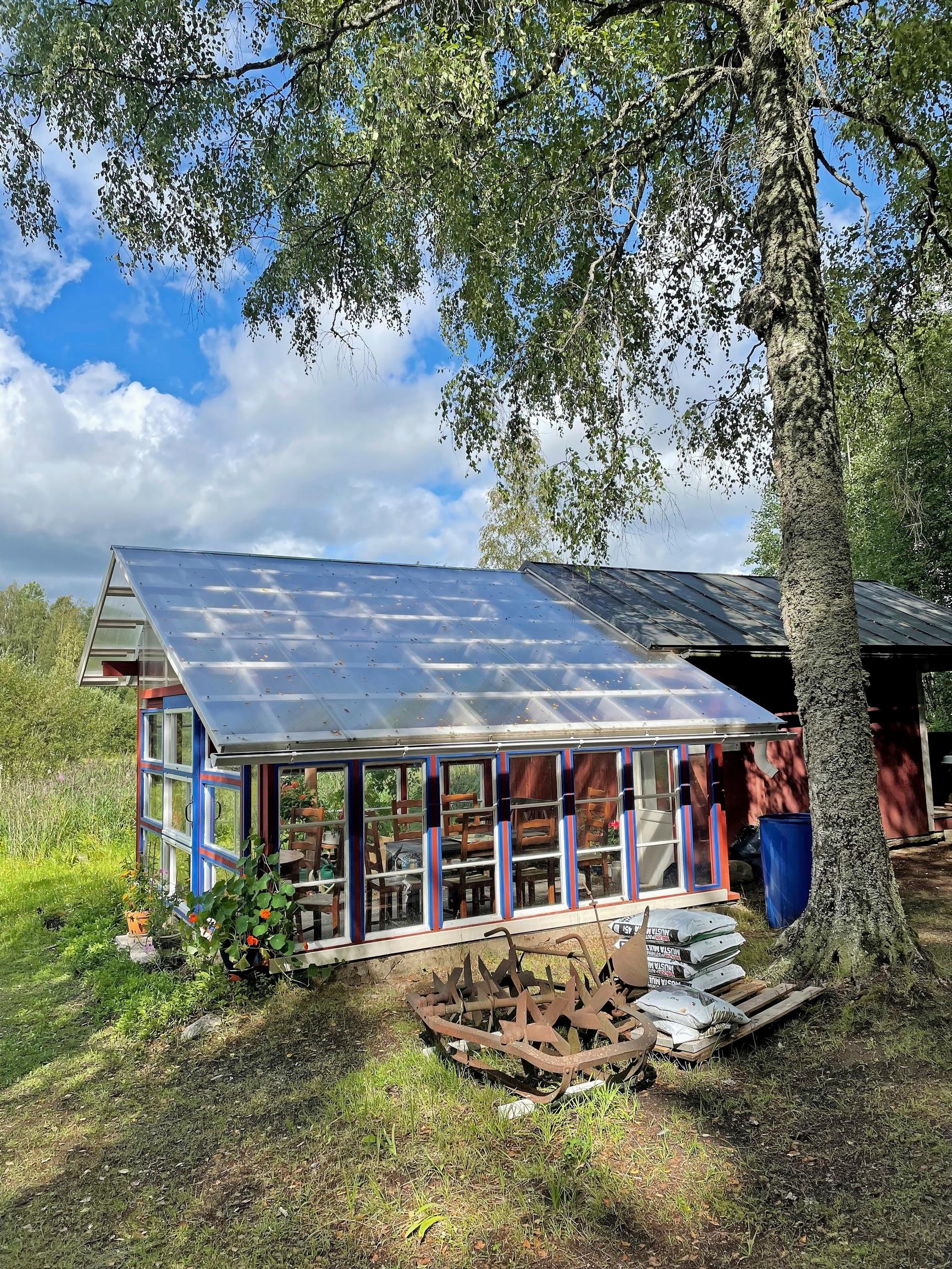 ikkunoista tehty pergola, jolla levyt katolla, vieressä punainen rakennus