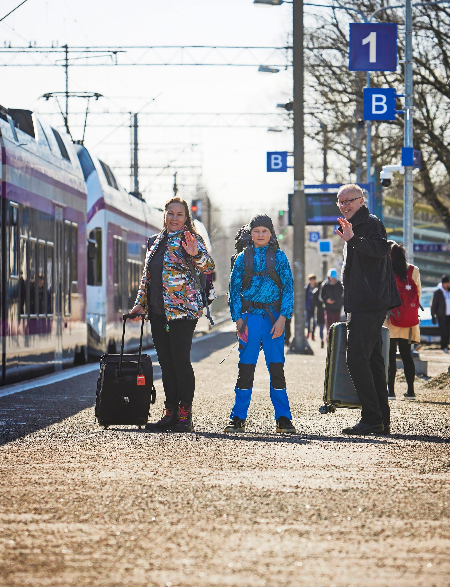 kolmihenkinen perhe juna-asemalla matkalaukkujen kera