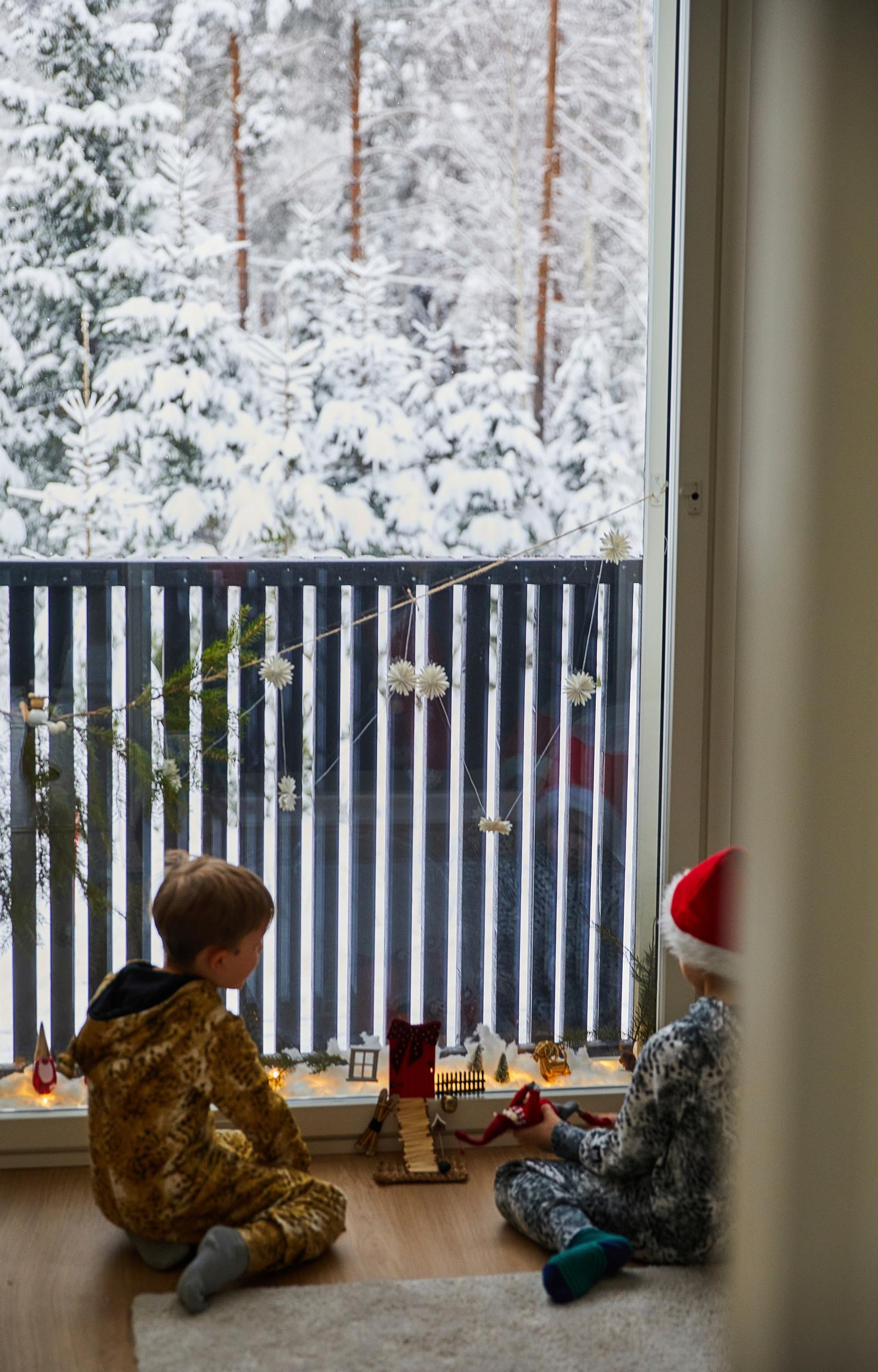 pikkupojat lattialla leikkimässä parvekkeen edessä, taustalla luminen metsä