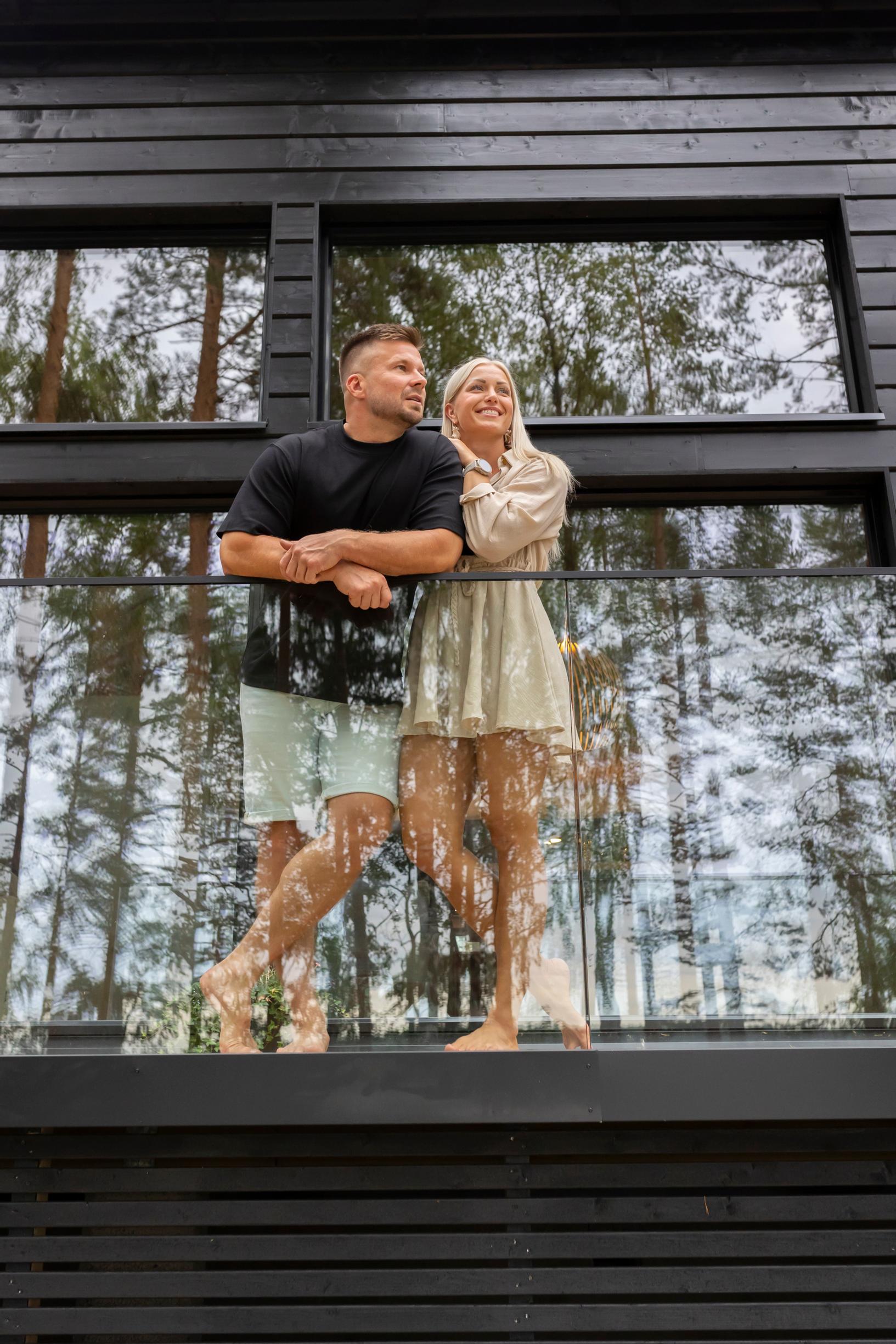 Pauliina Räisänen ja Vertti Harjuniemi vierekkäin mökkinsä terassin kaiteeseen nojaamassa