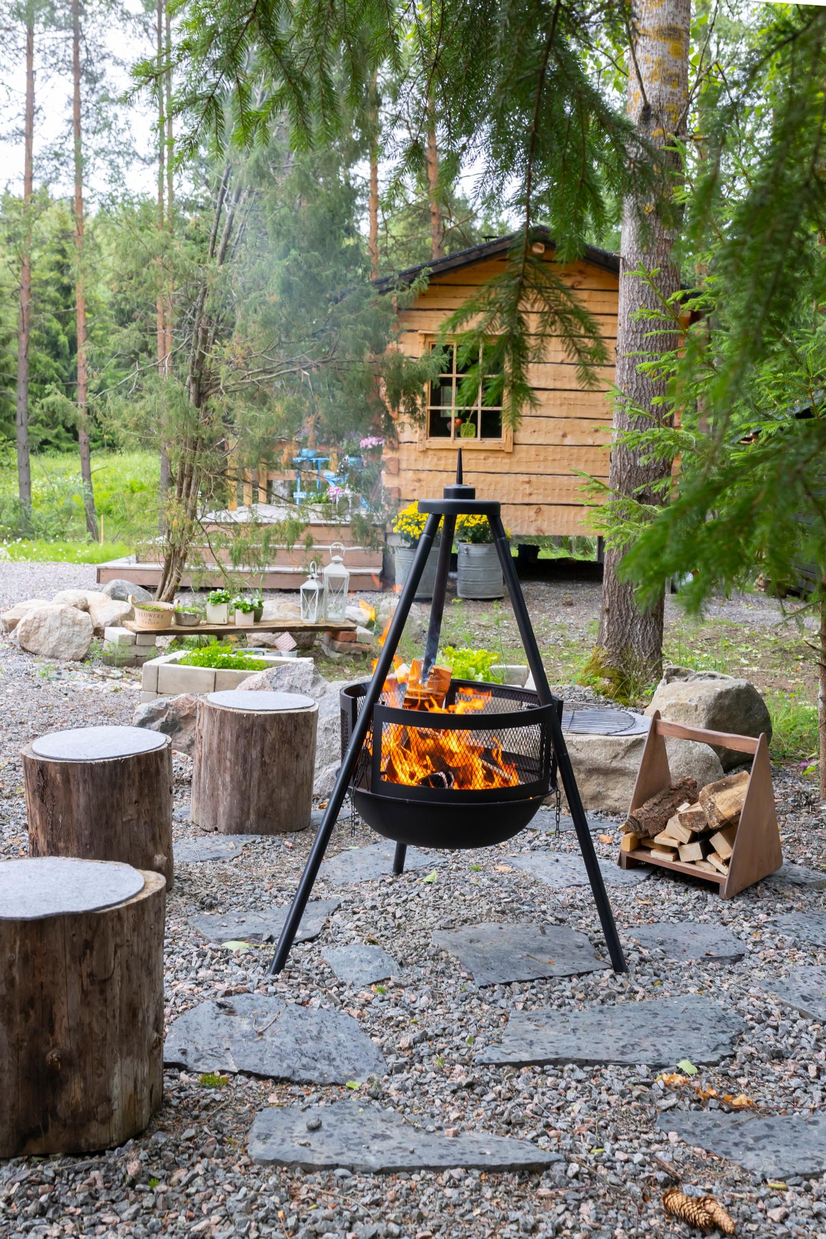 liuskekiviä, tulisijassa tuli ja pöllejä, taustalla hirsimökki