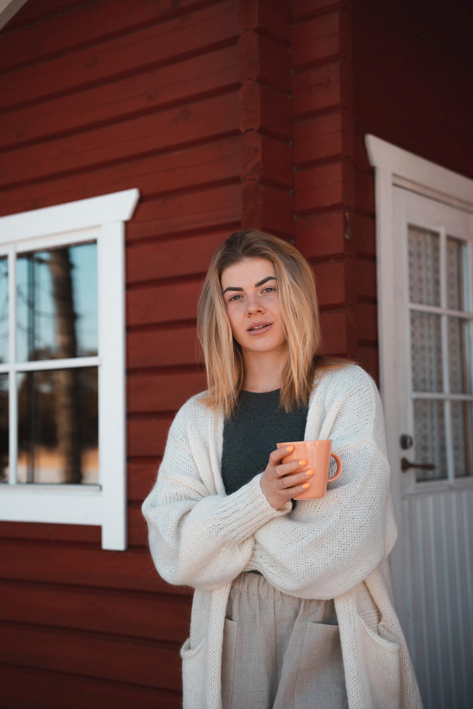 Pernilla Böckerman seisoo mökin edessä kahvikuppi kädessä