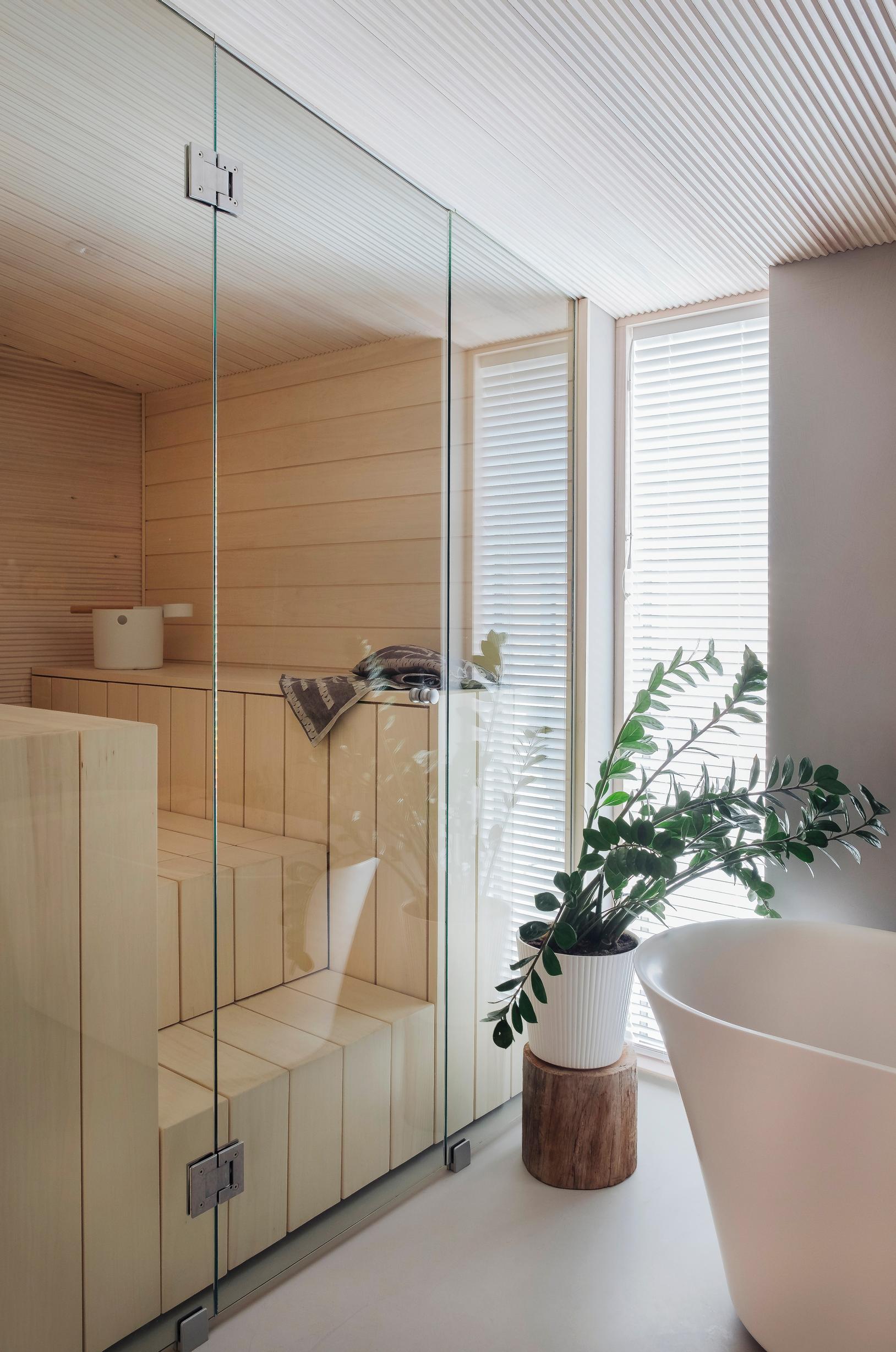Lasiseinäinen moderni, valkea sauna kylpytilassa, jossa ikkuna ja amme