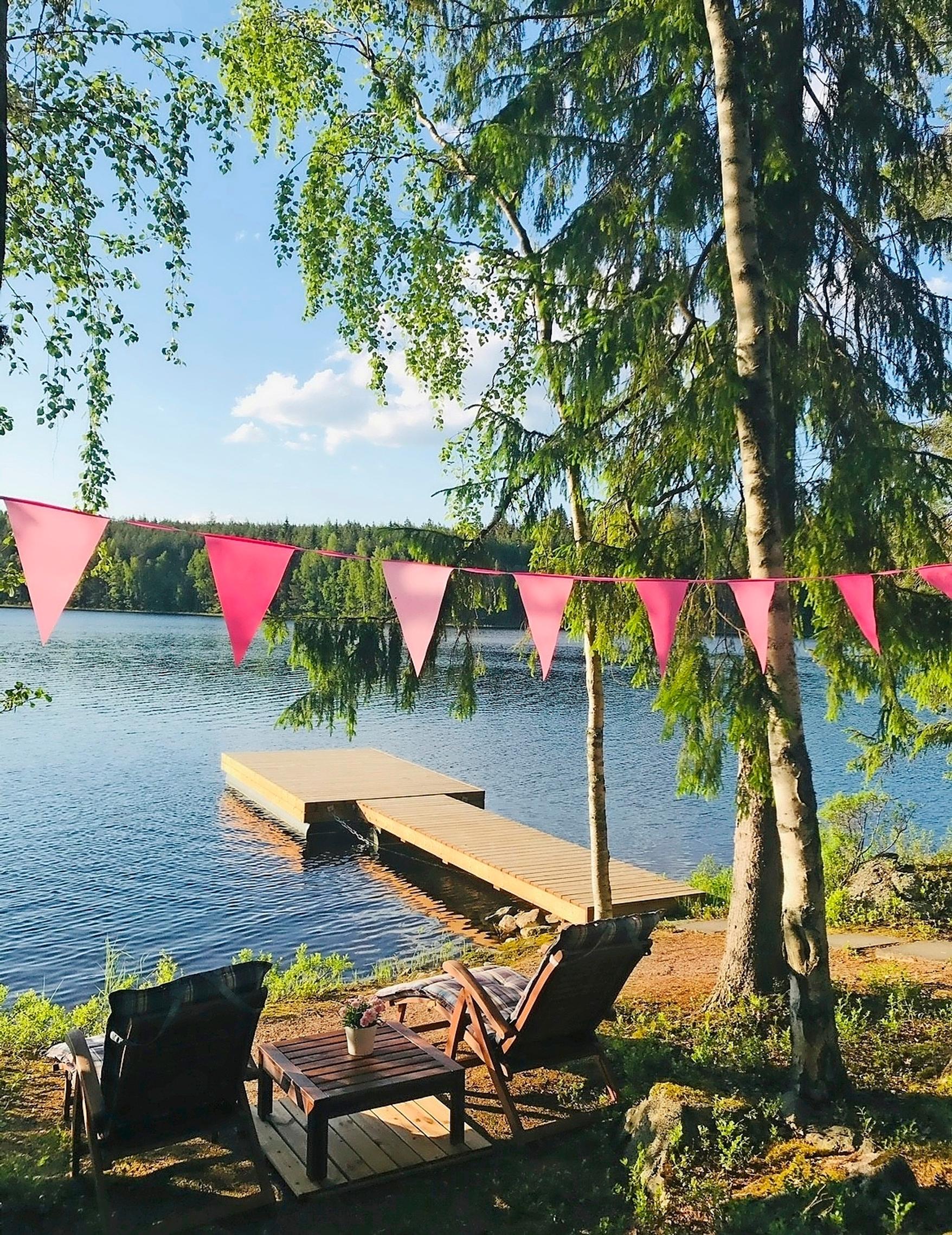 Näyttelijä Krisse Salmisen kesämökin rannassa aurinkotuolit ja pöytä, viirinauha ja laituri