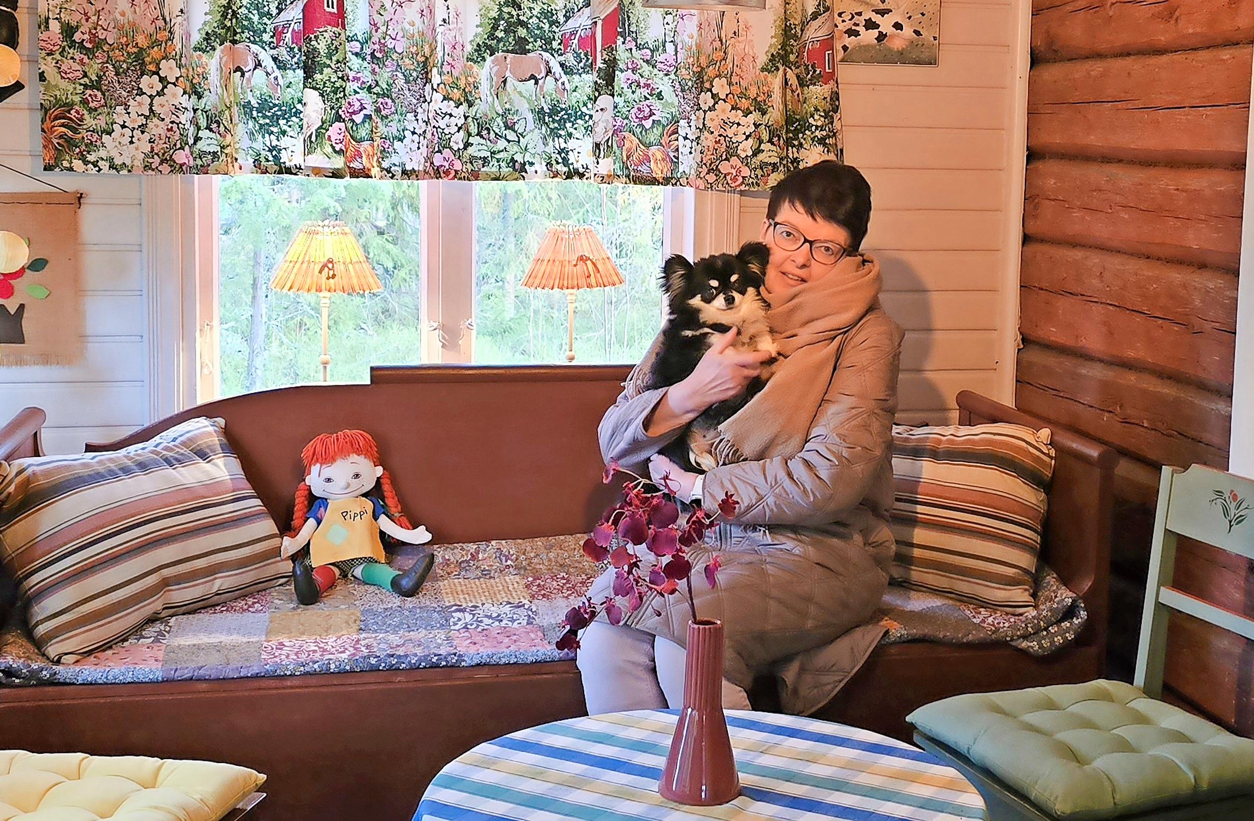 Anne Suomäki mummonmökin vanhalla sohvalla pieni koira sylissään