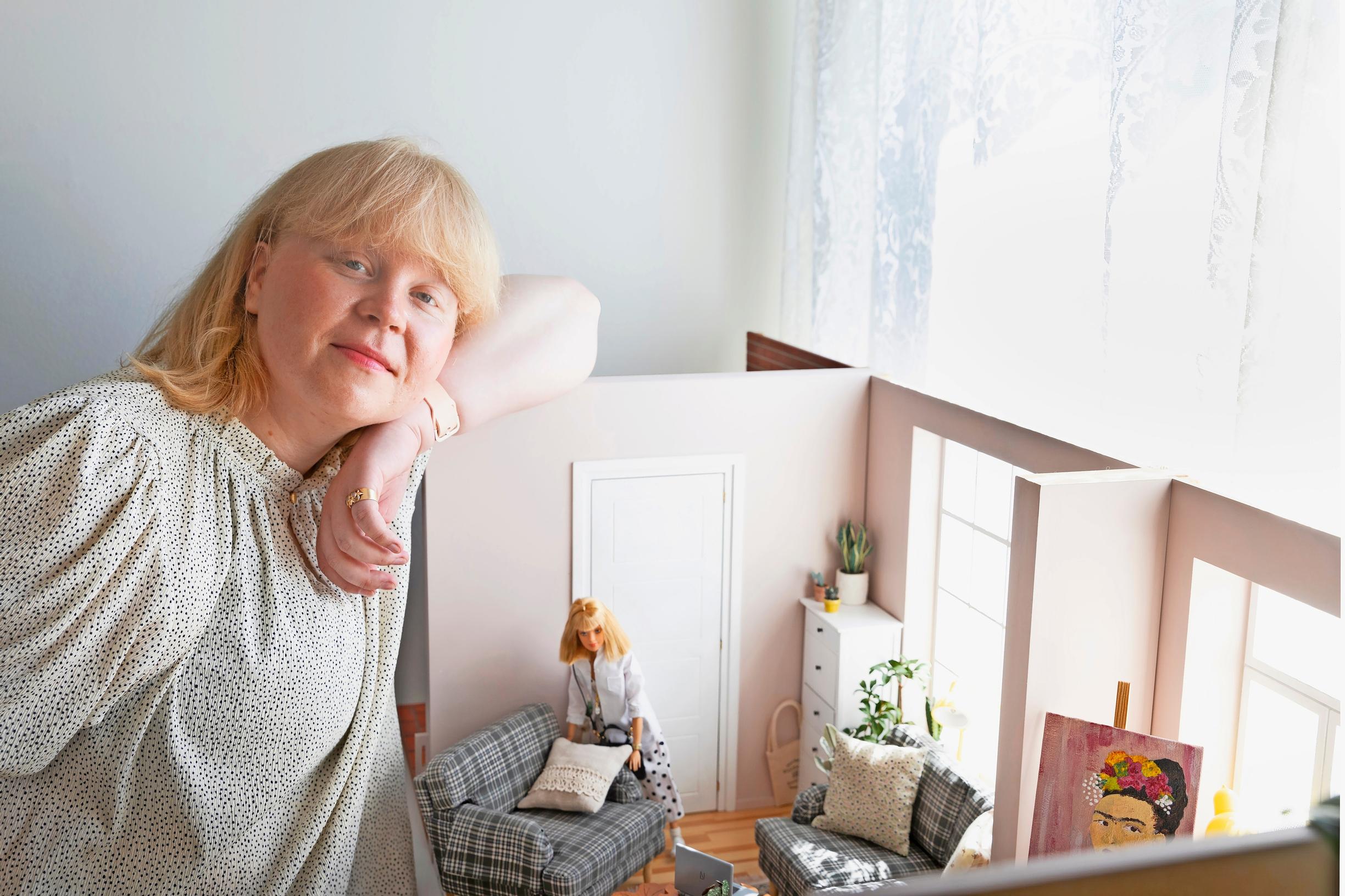 nainen nojaa nukkekotiin, jonne on rakentanut olohuoneen Barbie-nukelle