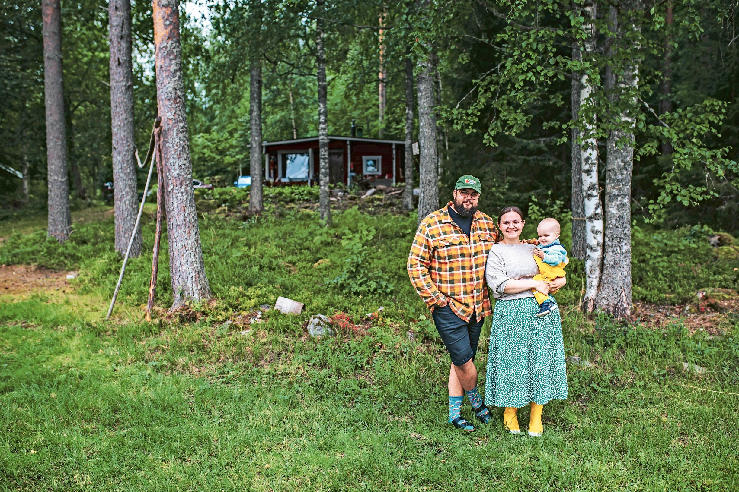 Isä ja äiti pikkupoika sylissä mökin edessä.