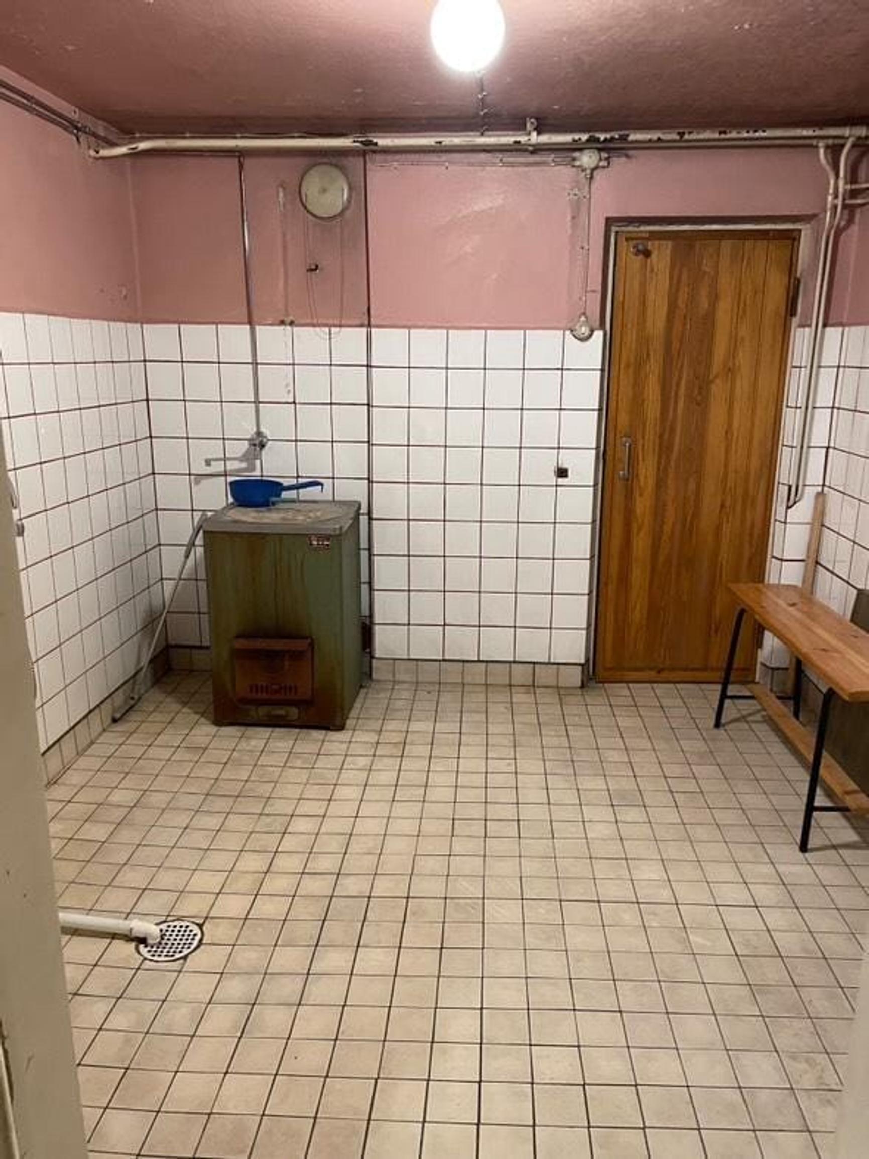 Kylpyhuoneessa on ruskeansävyinen laattalattia, reilun metrin korkeuteen laatoitetut valkoiset seinät ja vaaleanpunaiseksi maalatut seinien yläosat.