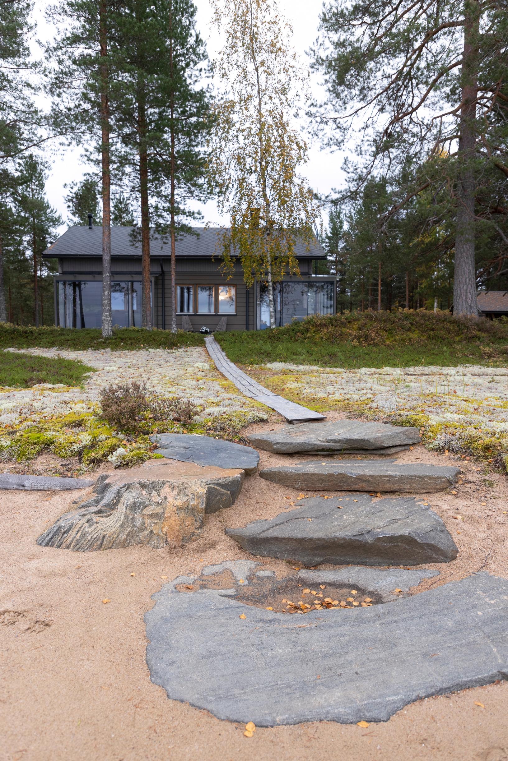 isoja kiviä rantahiekalla ja niiltä pitkospuut mökille, taustalla metsää