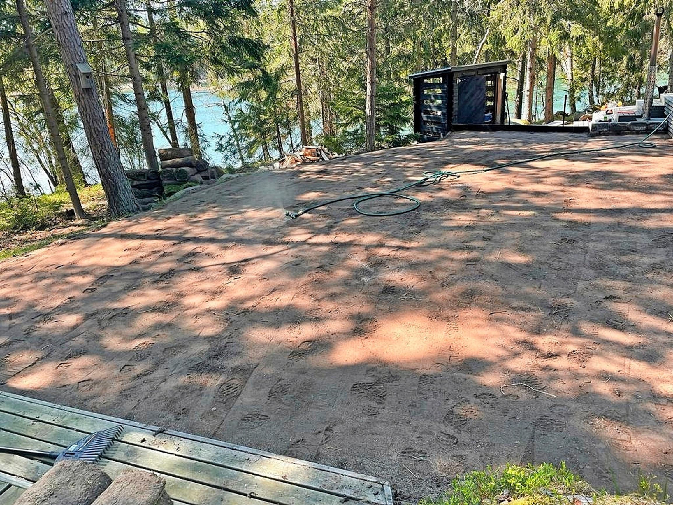 iso sorakenttä, kasteluletku, puukatos ja metsää järven edessä