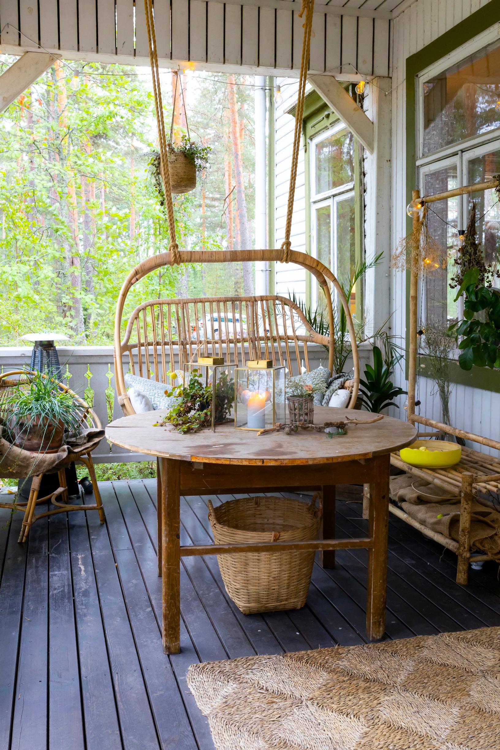 Huvilan terassilla riippuva rottinkituoli, pyöreä pöytä ja lyhtyjä.