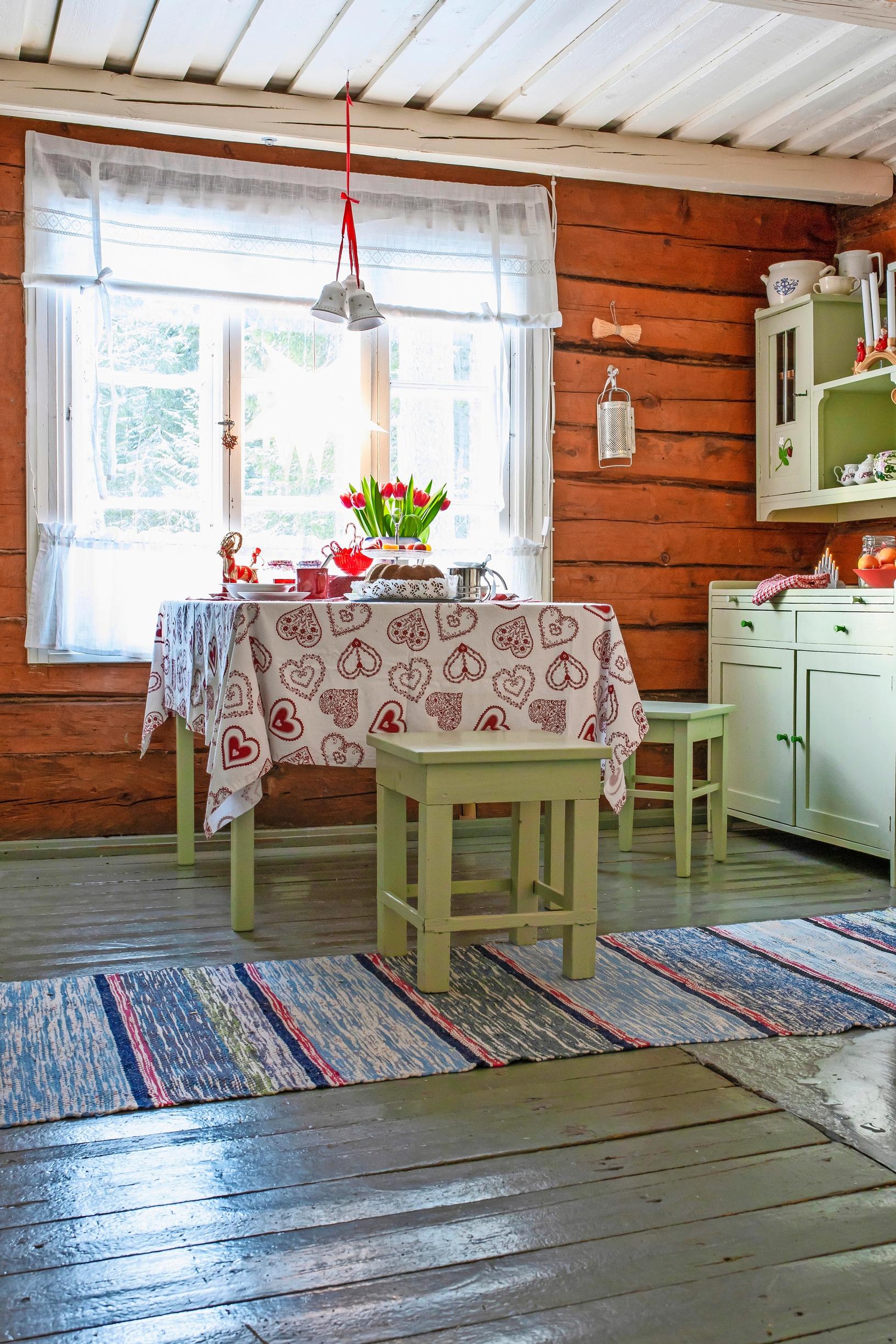 Punavalkoinen pöytäliina vihreäksi maalattujen keittiökalusteiden seurassa.