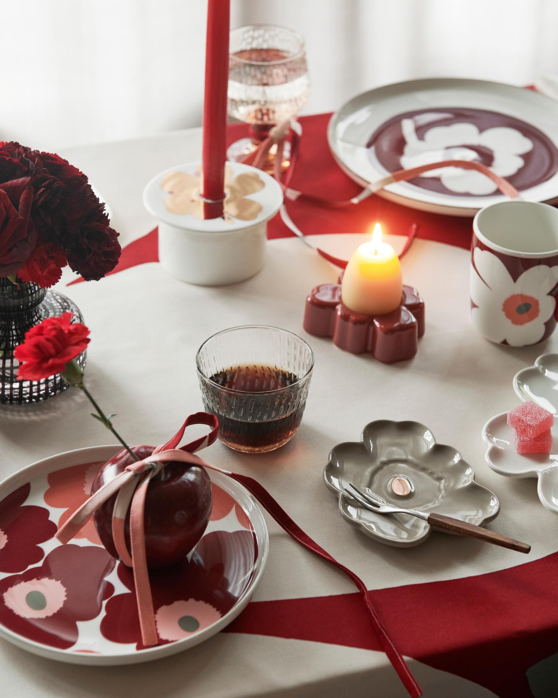 Marimekon Unikko-astioita pöydässä, punaista ja valkoista, kynttilä palamassa