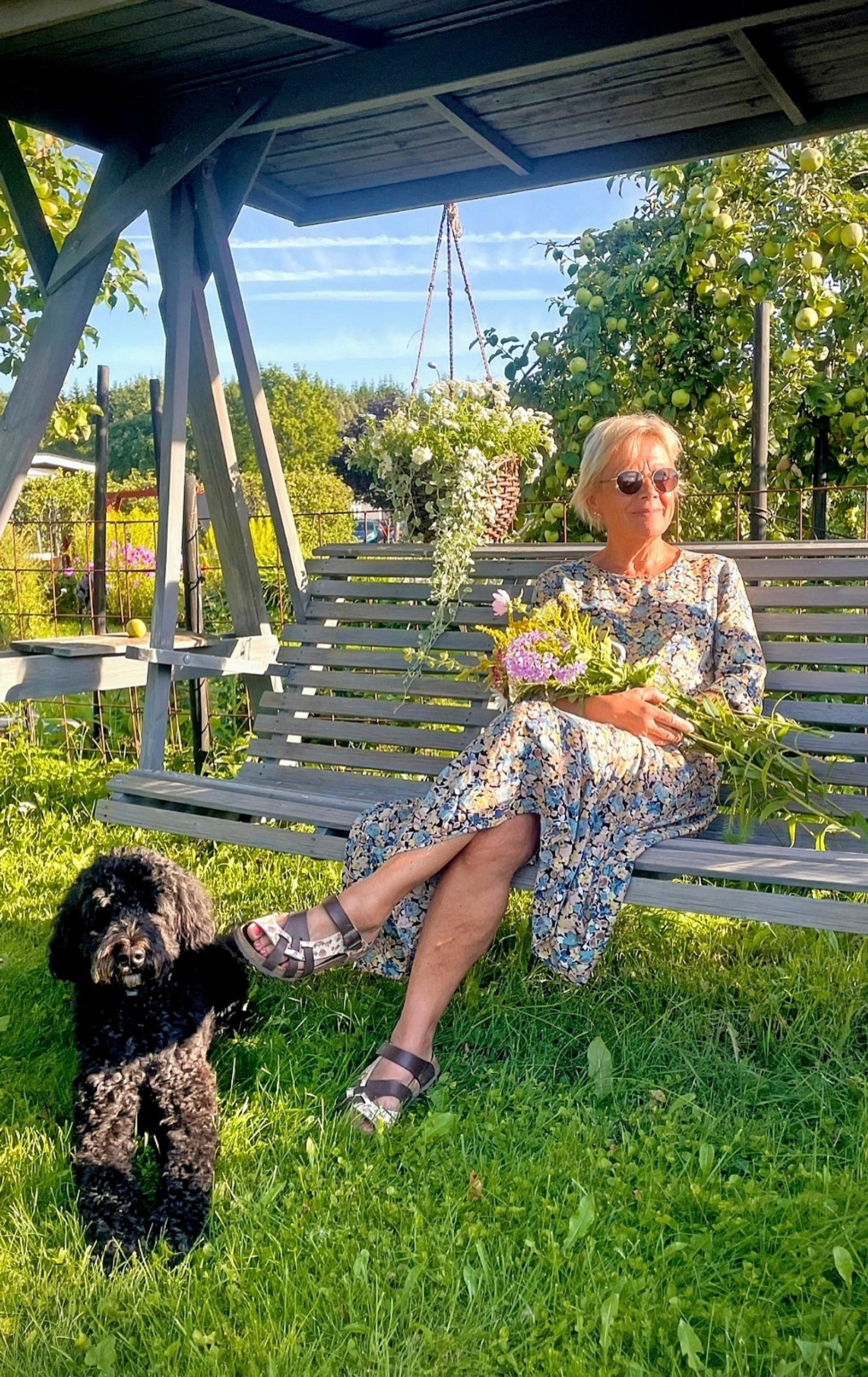 Ulla Hyytiäinen istuu puutarhakeinussa, vieressä koira