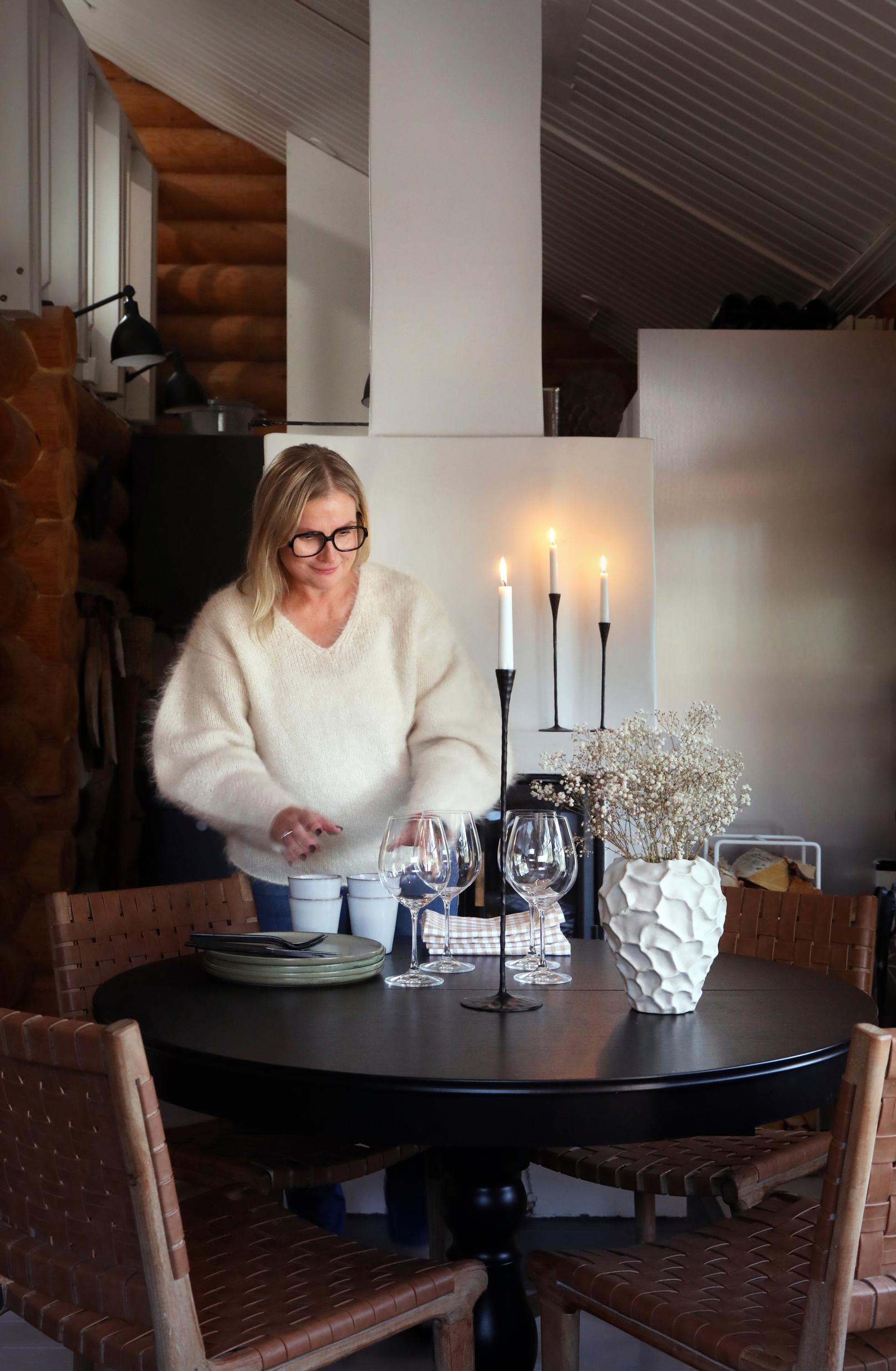 Teija Sääksmäki kattaa pyöreää pöytää, jolla palaa kynttilöitä 