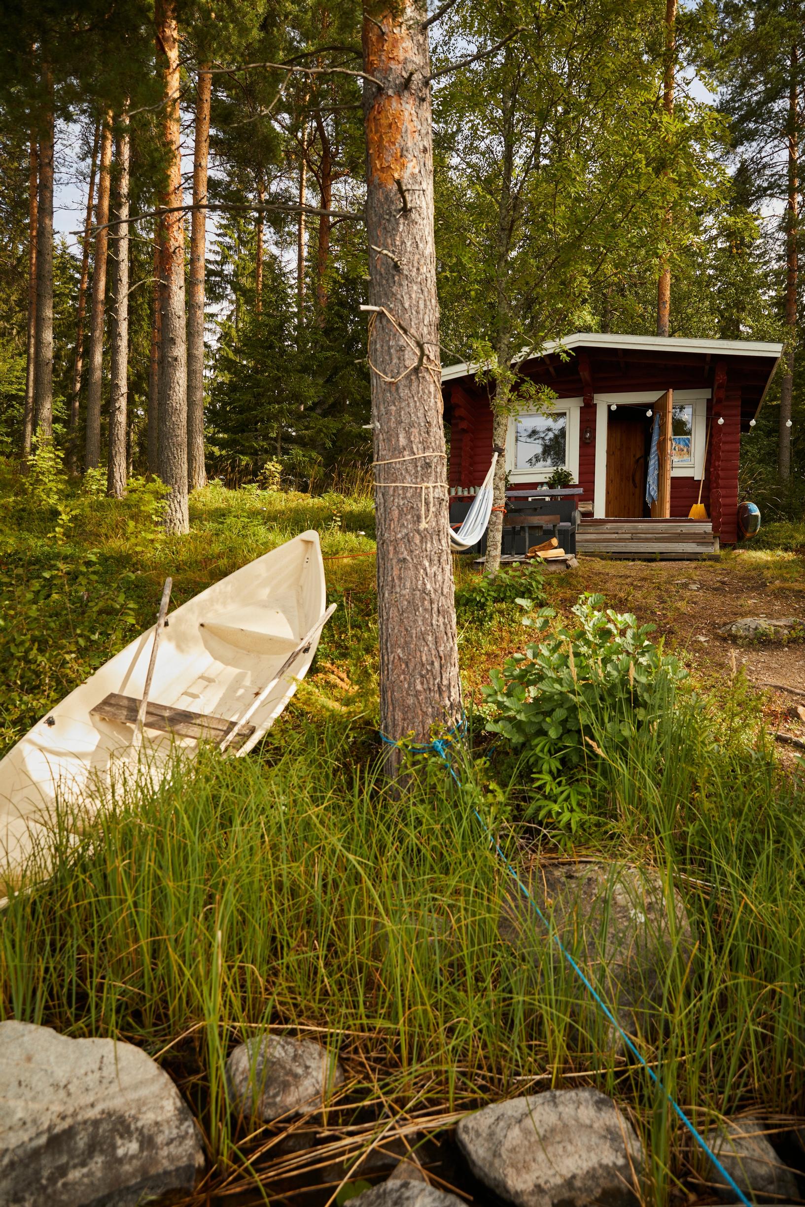 Pieni punainen rantasauna metsän reunassa, rannassa soutuvene.