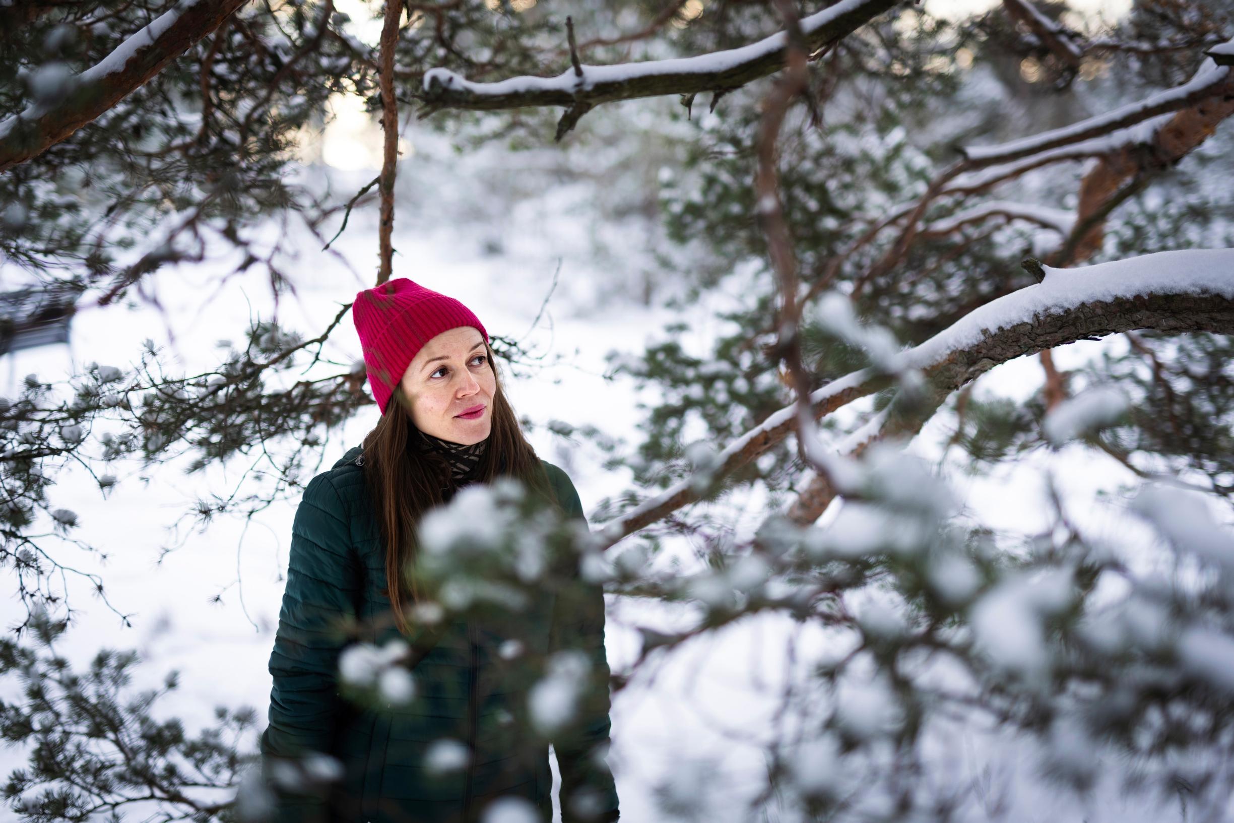 nainen seisoo talvisessa metsässä männyn takana