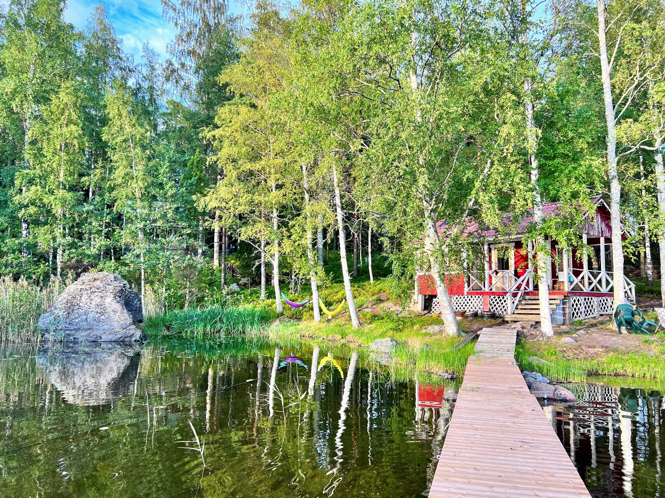 punainen rantasauna tyynen järven rannassa, pitkä laituri ja metsää