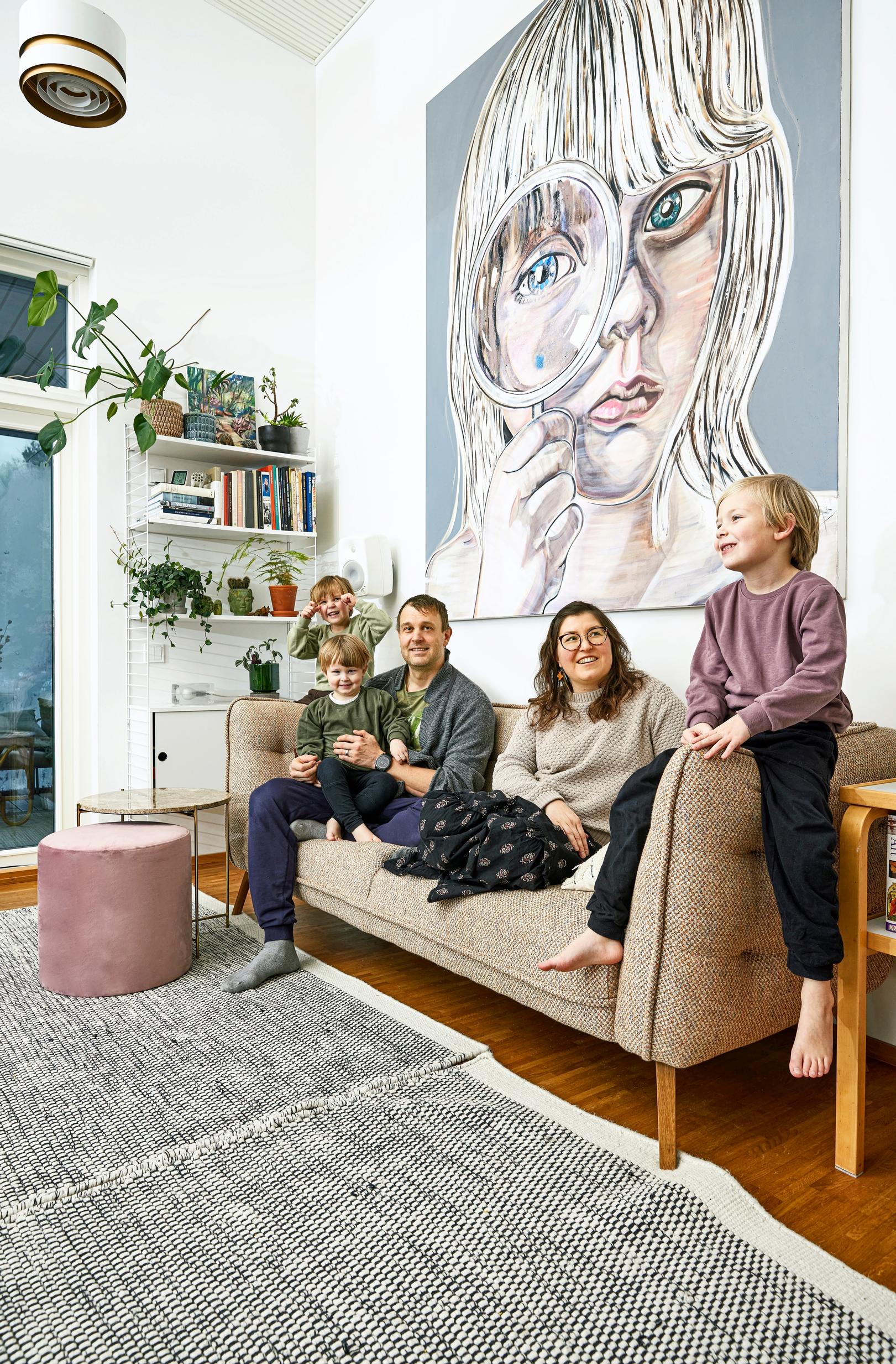 Puhakan perhe kotisohvalla, taustalla Leena Nion Girl-teos