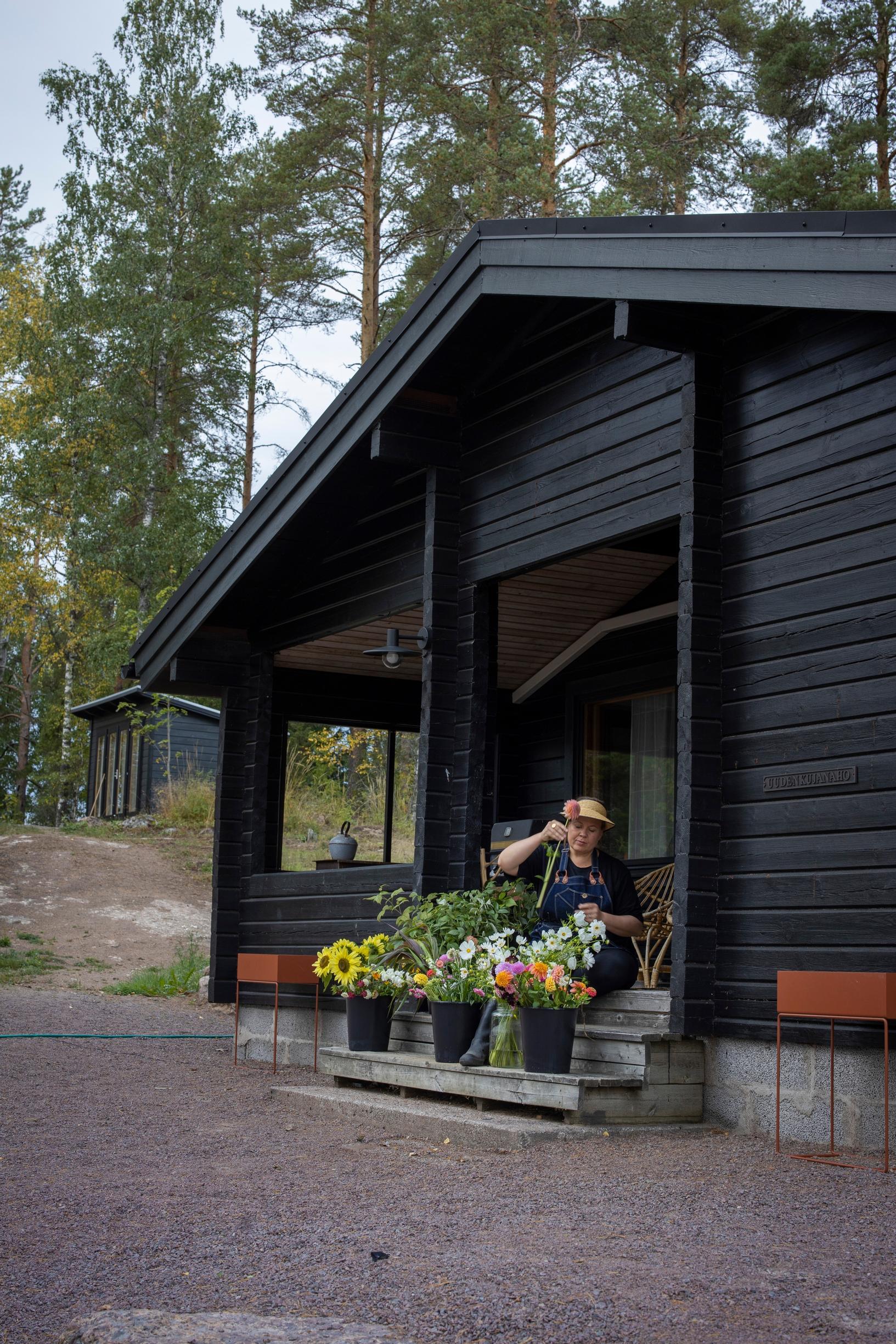 Nainen lajittelee kukkia mökin rappusilla.